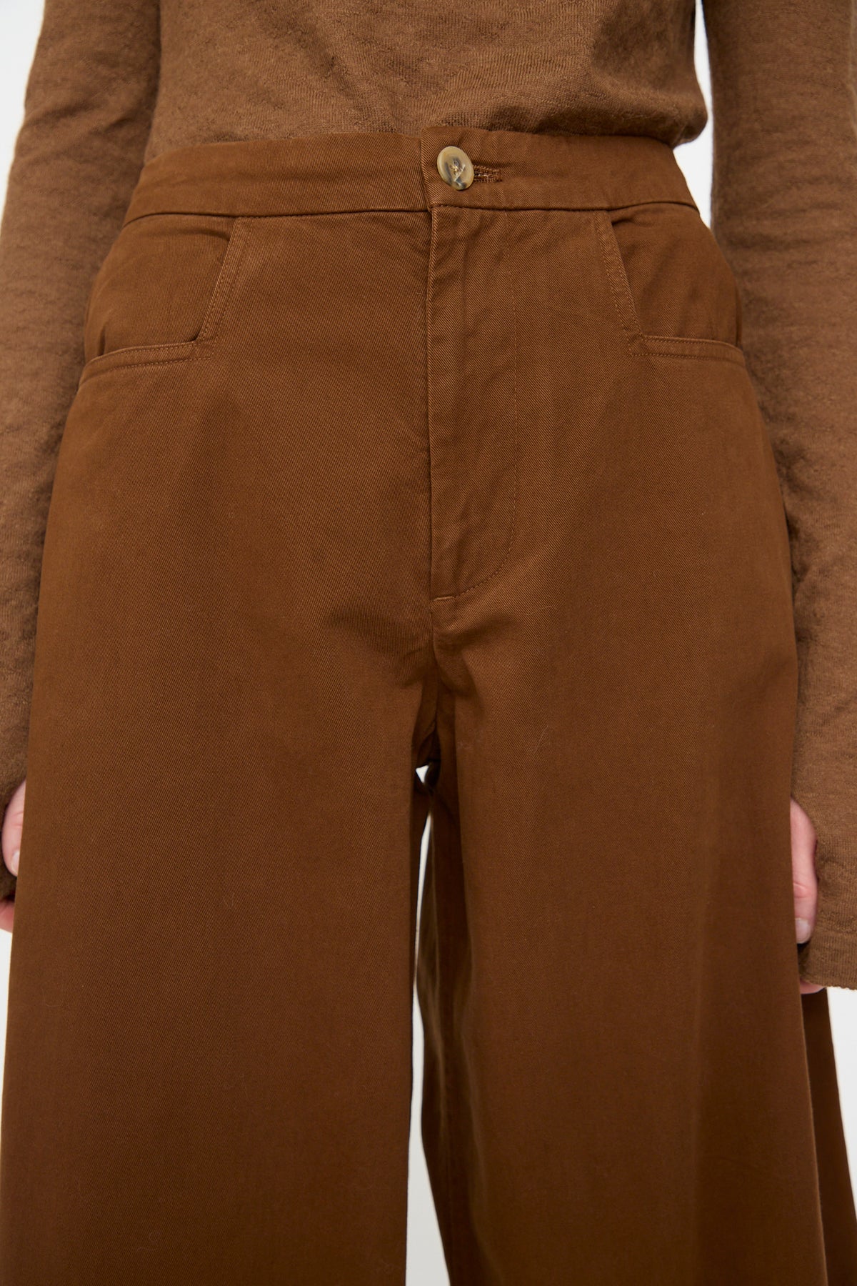 Model wearing the Lauren Manoogian Sweep Pants in Rust—relaxed fit, wide-leg cotton pants—paired with a brown long-sleeve top; shown from waist to mid-thigh with hands at sides.