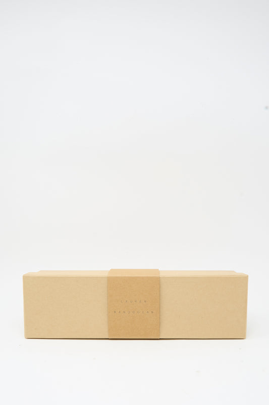 A rectangular, closed cardboard box with a minimalist design and a centered paper band, placed against a plain white background—perfect for gifting the Lauren Manoogian Tall Sock Set in Mix, premium baby alpaca socks made in Peru.