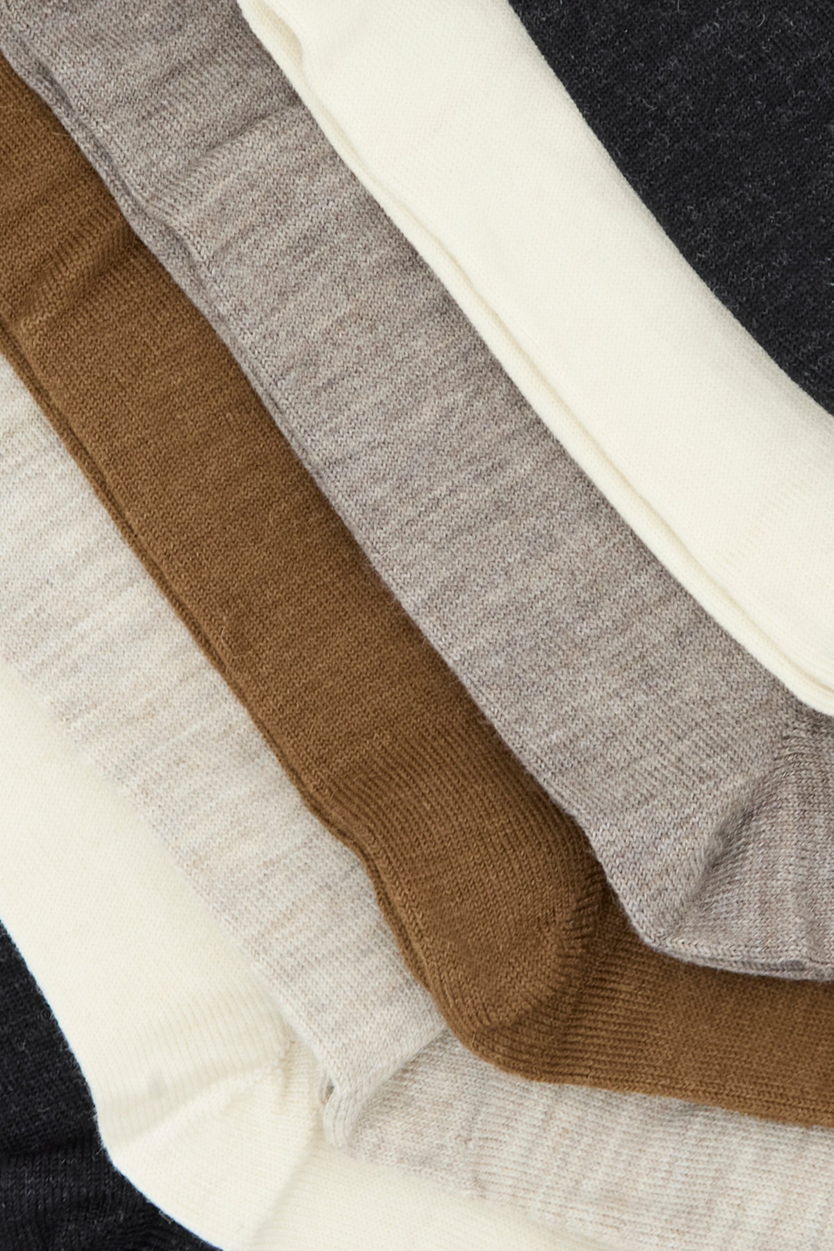 Five pairs of socks in beige, brown, cream, and gray tones are neatly stacked in an overlapping arrangement on a flat surface. The Tall Sock Set in Mix by Lauren Manoogian, crafted from cozy baby alpaca and made in Peru, offers a soft and luxurious feel perfect for everyday comfort.