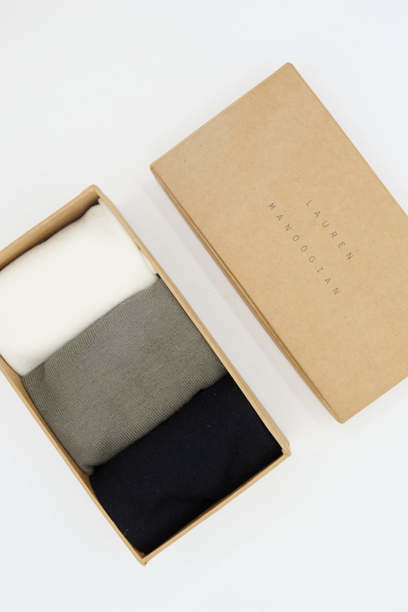 A cardboard box labeled "Lauren Manoogian" holds three pairs of Tall Socks in Mix—white, gray, and black. The box, made in Peru, is open with the lid placed beside it.