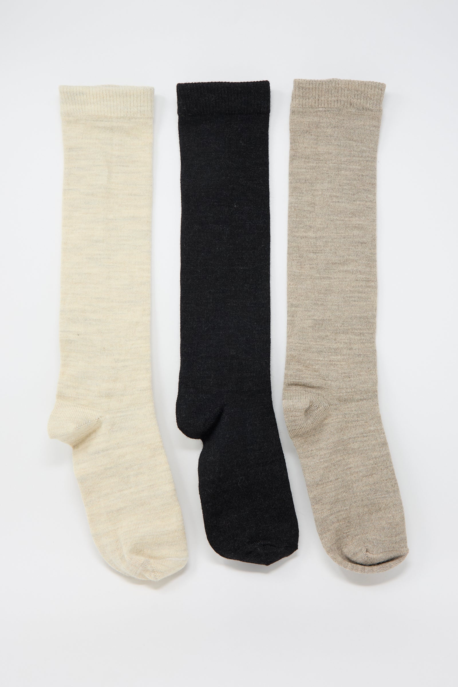 Three knee-length socks in cream, black, and beige are laid out side by side on a plain white background, showcasing the luxurious Tall Socks in Mix pack of three from Lauren Manoogian, made from an alpaca blend.