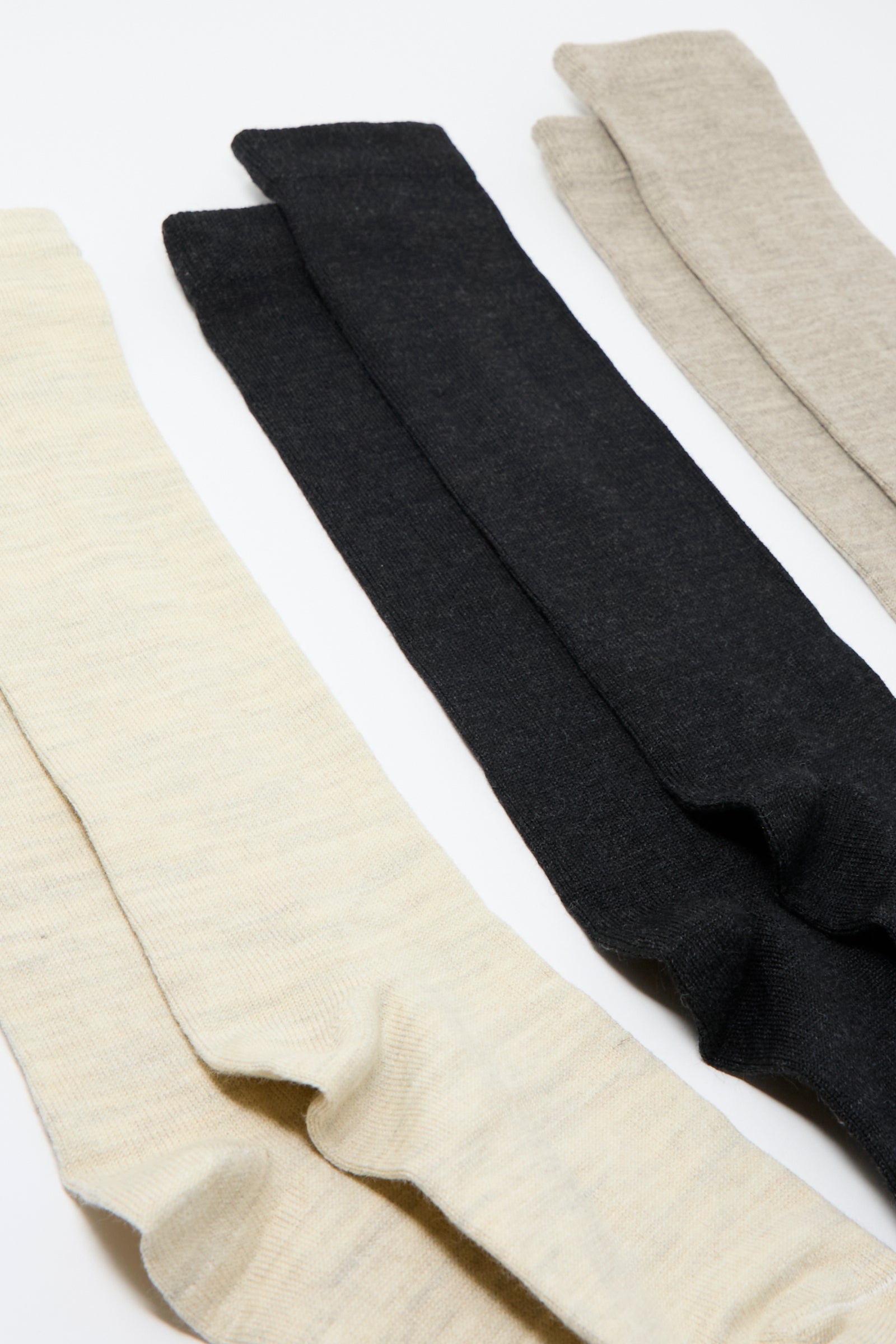 Four pairs of Lauren Manoogian Tall Socks in Mix, available in beige, light beige, black, and light gray, are laid out overlapping each other on a white surface. These luxurious socks feature a soft alpaca blend for extra comfort and warmth.