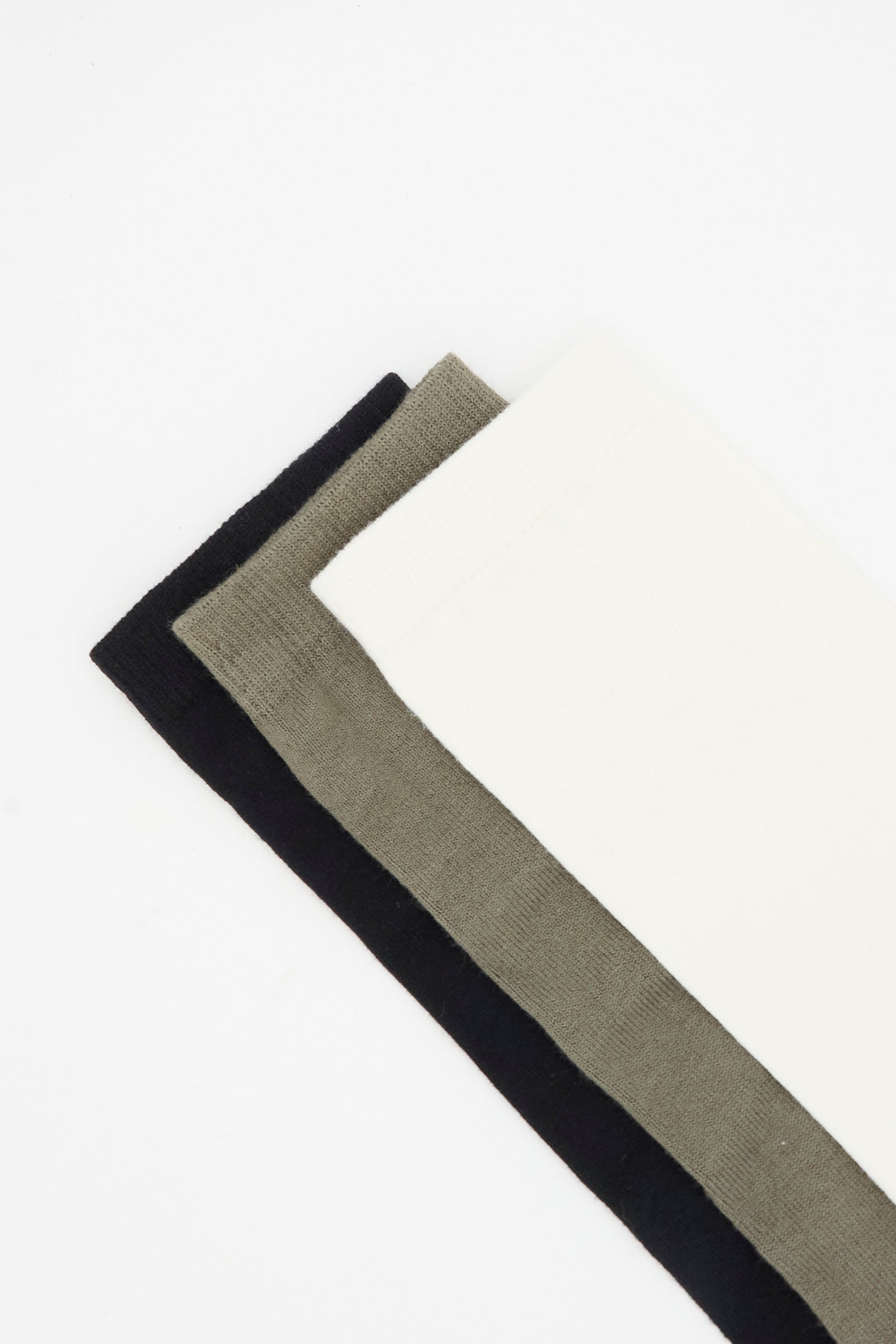 Three pairs of Tall Socks in Mix by Lauren Manoogian—black, olive green, and white—are laid out side by side on a white background. Made in Peru, these cozy alpaca wool socks offer comfort and quality craftsmanship.