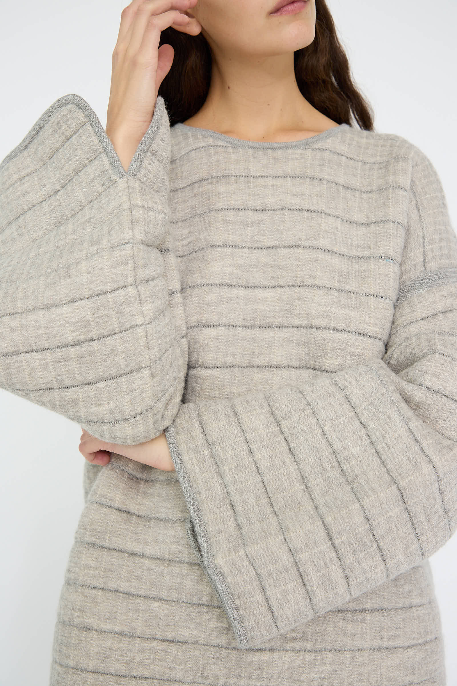 The individual is wearing the Tami Pullover in Grey Melange by Lauren Manoogian, a textured long-sleeve top with pronounced wide sleeves and a relaxed fit, made in Peru.