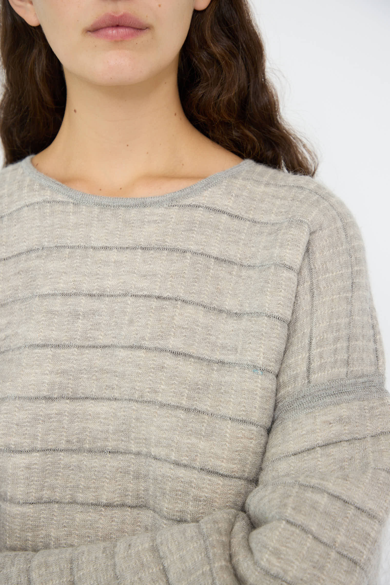 A person wearing the Tami Pullover in Grey Melange with arms crossed—crafted from quilted knit alpaca for that relaxed fit. Only the lower face is visible. The pullover is by Lauren Manoogian.