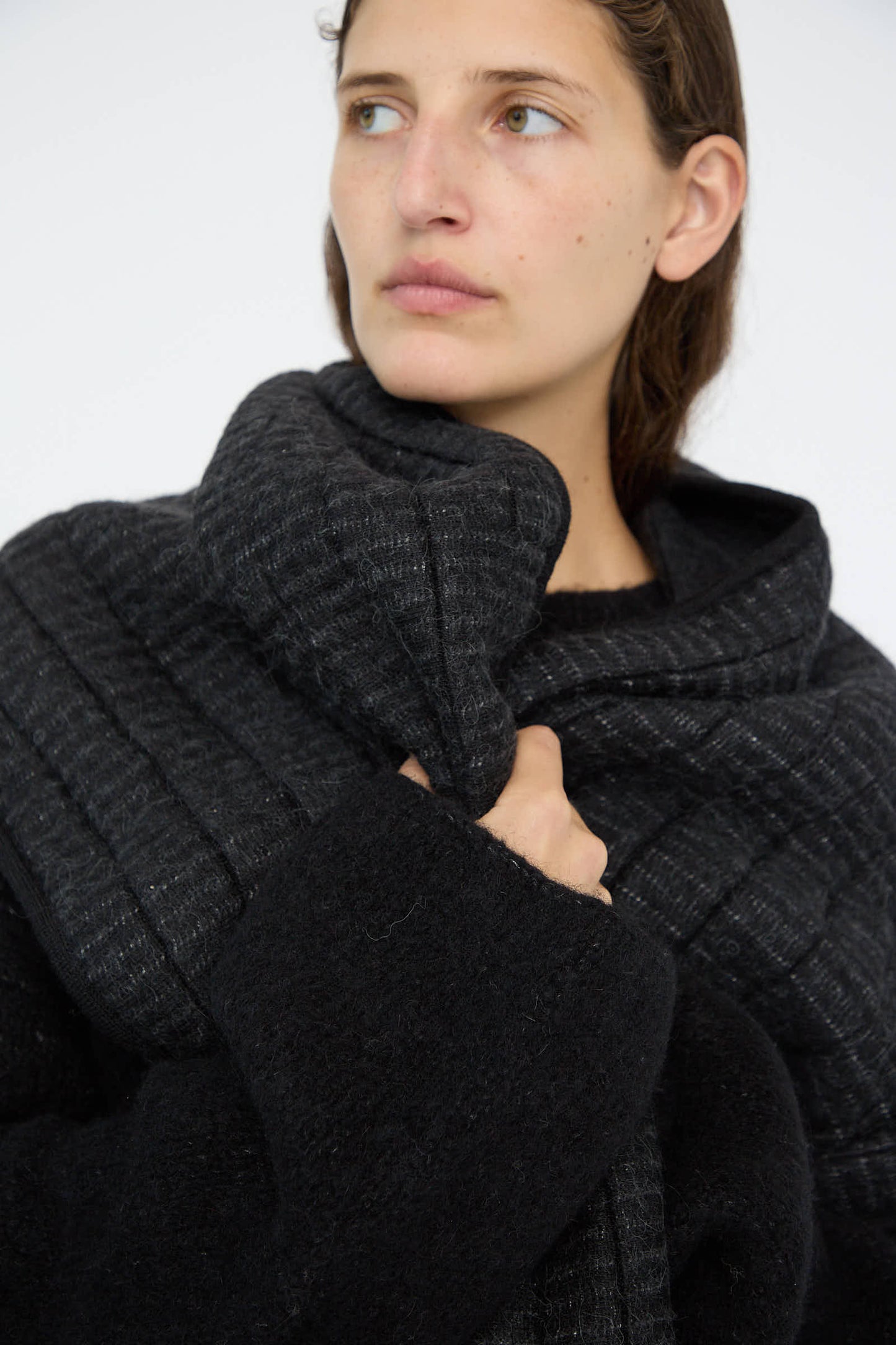 A person wearing the Tami Wrap in Black by Lauren Manoogian, featuring a high collar and crafted from an exquisite alpaca blend, looks to the side against a plain background.