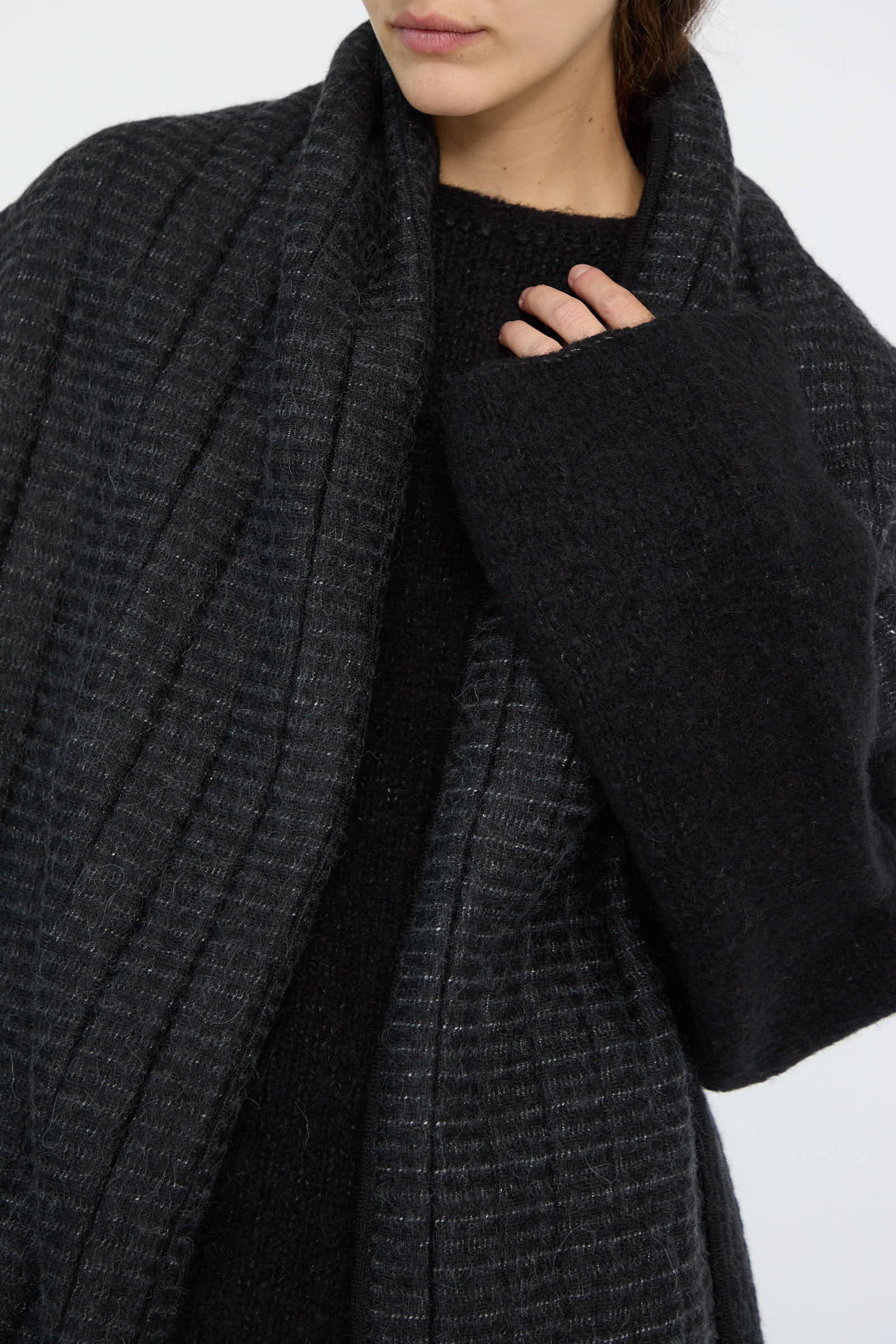 A person wearing the Tami Wrap in Black by Lauren Manoogian, crafted in Peru, is shown from the chest down over a black sweater, with their left hand slightly visible.