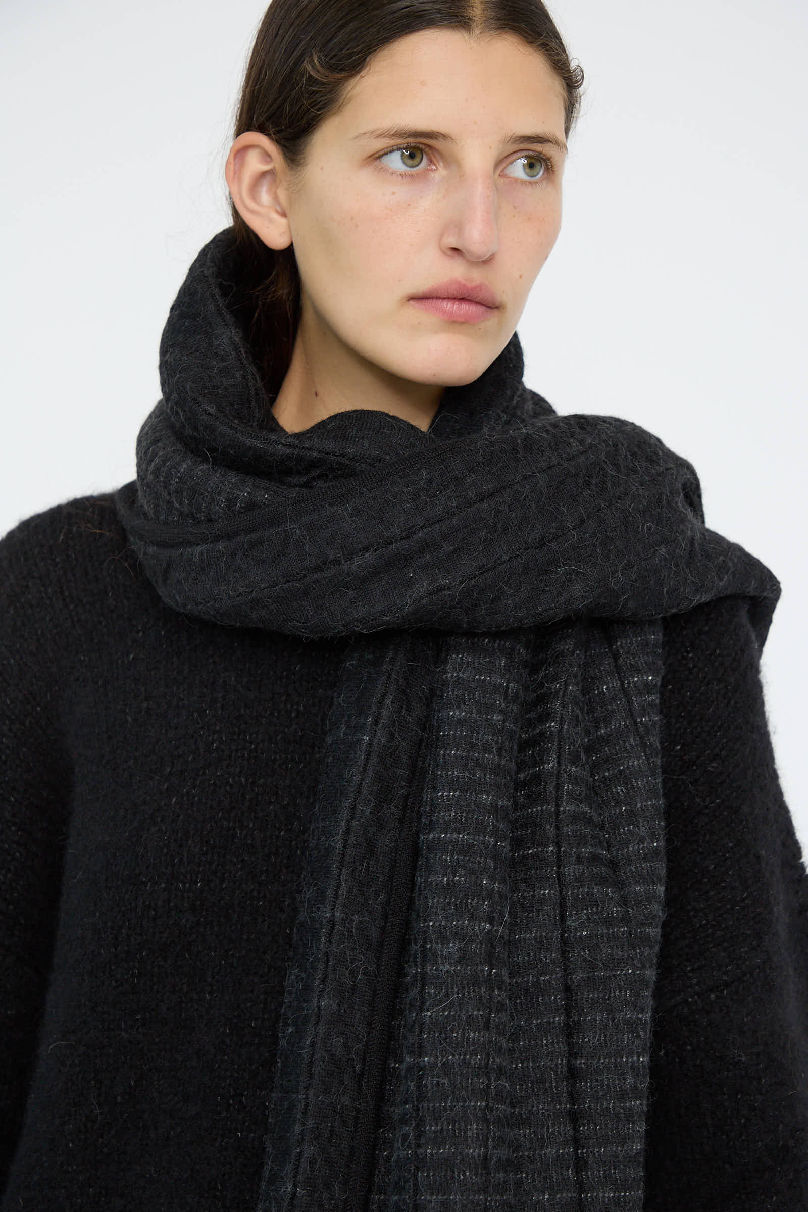 A person wearing a black alpaca blend sweater and the Tami Wrap in Black by Lauren Manoogian, looking to the side.