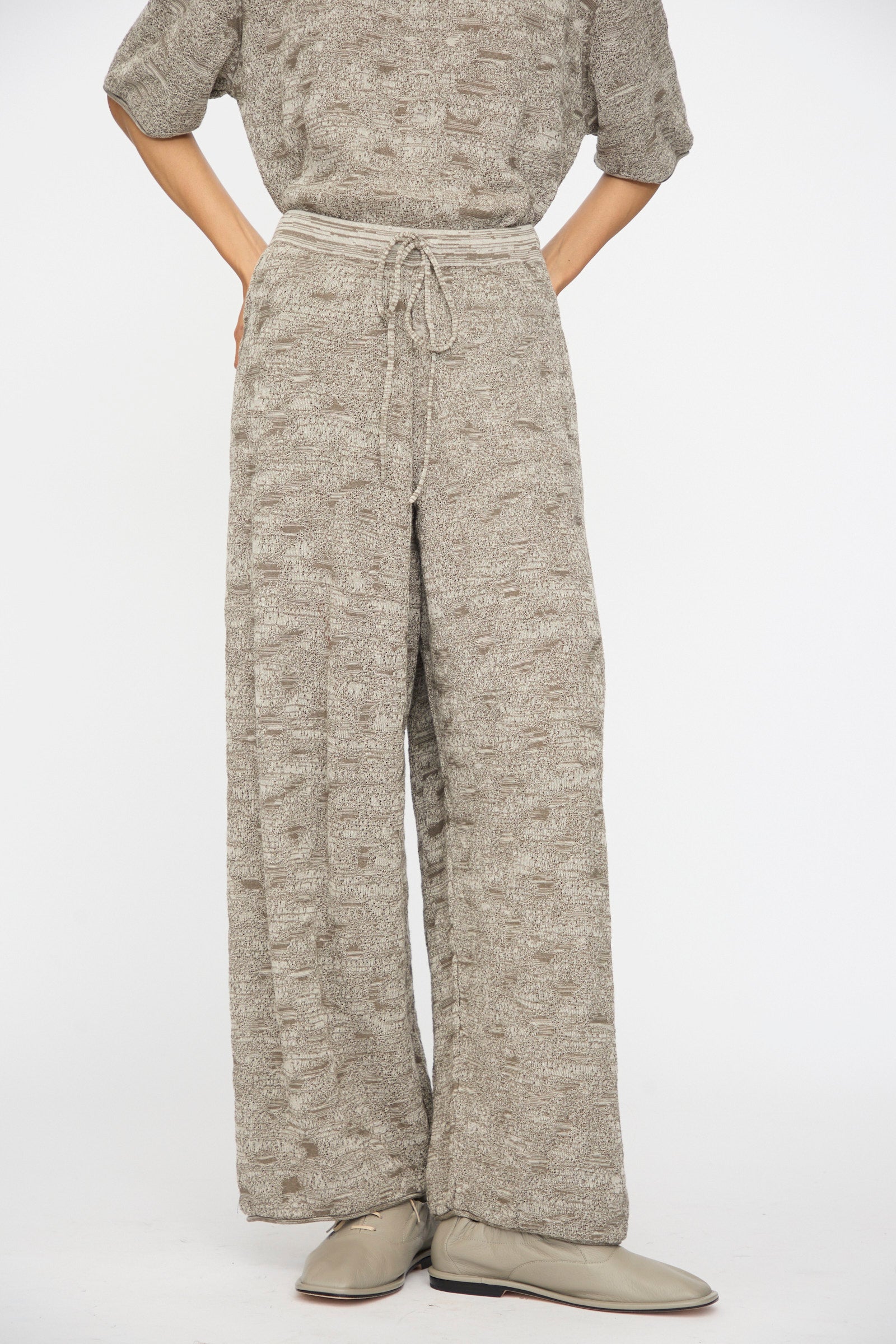 A person wears Lauren Manoogian's Terra Pants in Rock Marl, a textured, loose-fitting matching set with relaxed, elastic waist and drawstring pants, paired with beige shoes.