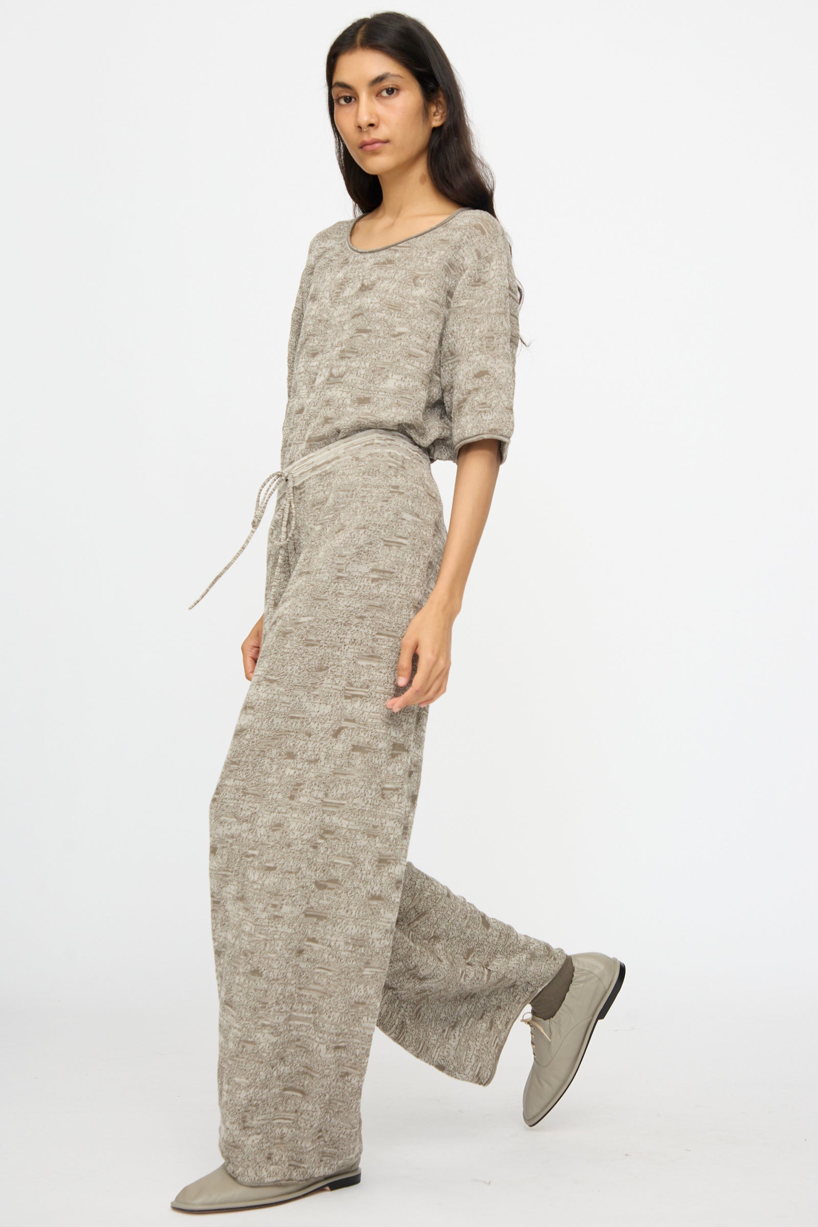 Person stands against a plain background wearing Lauren Manoogian's Terra Pants in Rock Marl—textured, loose-fitting pants with an elastic waist, styled with matching shoes for an effortlessly comfortable look.