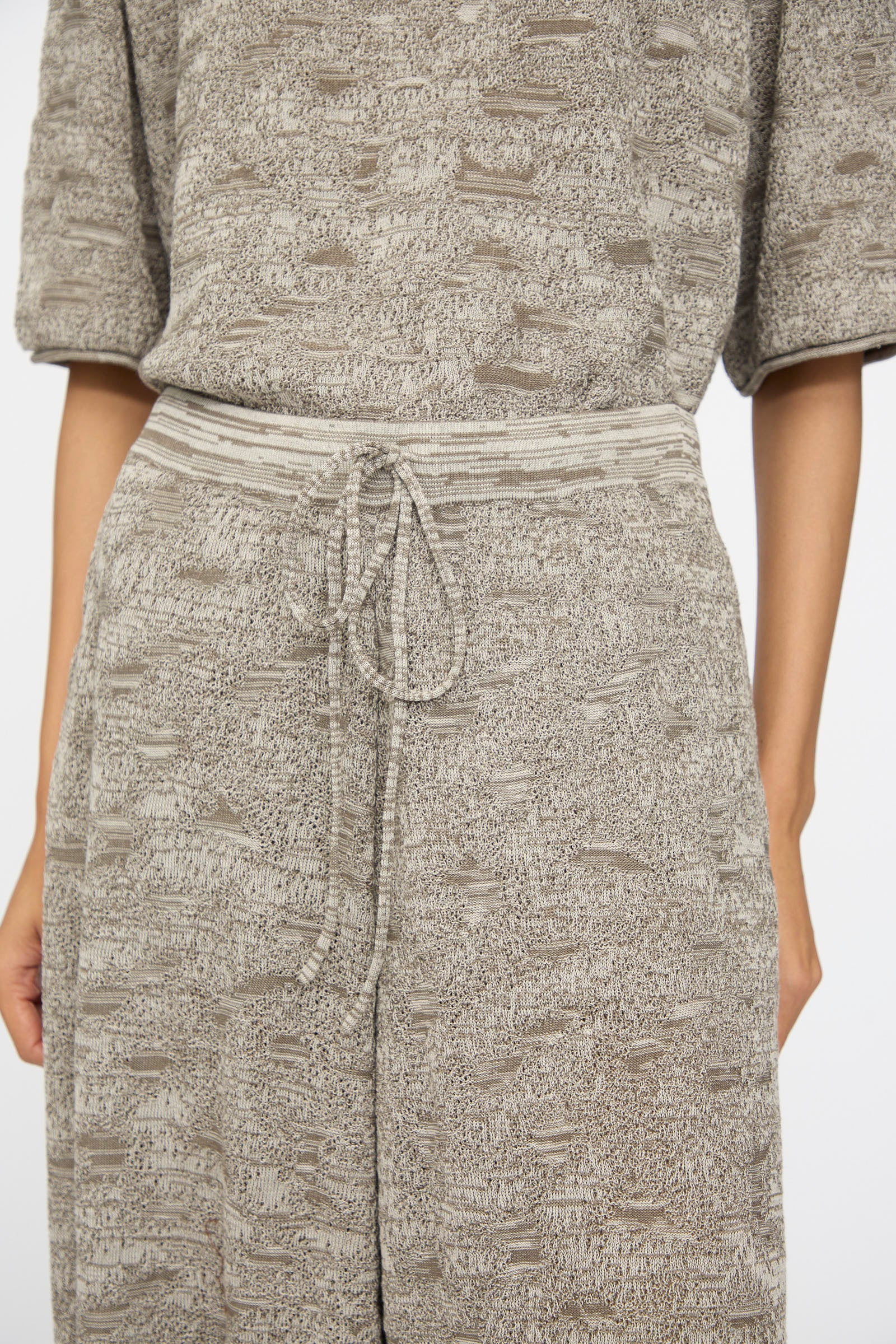 Close-up of a person wearing Lauren Manoogian's Terra Pants in Rock Marl, a textured light brown two-piece with relaxed pants featuring an elastic waist and drawstring.