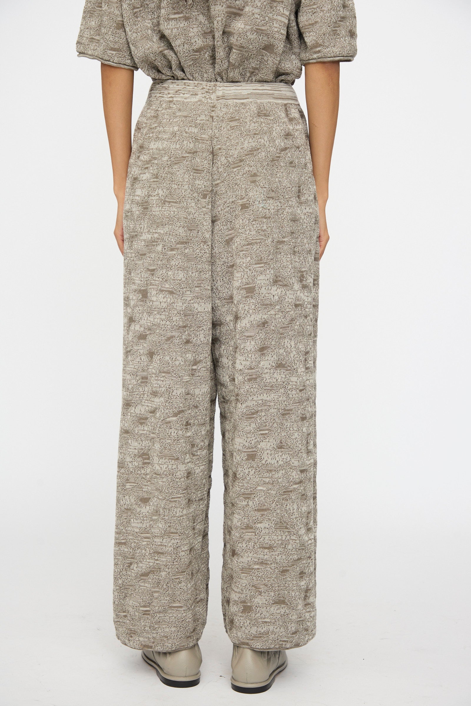 The lower half of a person is shown wearing the Lauren Manoogian Terra Pants in Rock Marl—textured, loose-fitting taupe pants with an elastic waist—paired with a matching top against a plain white background.