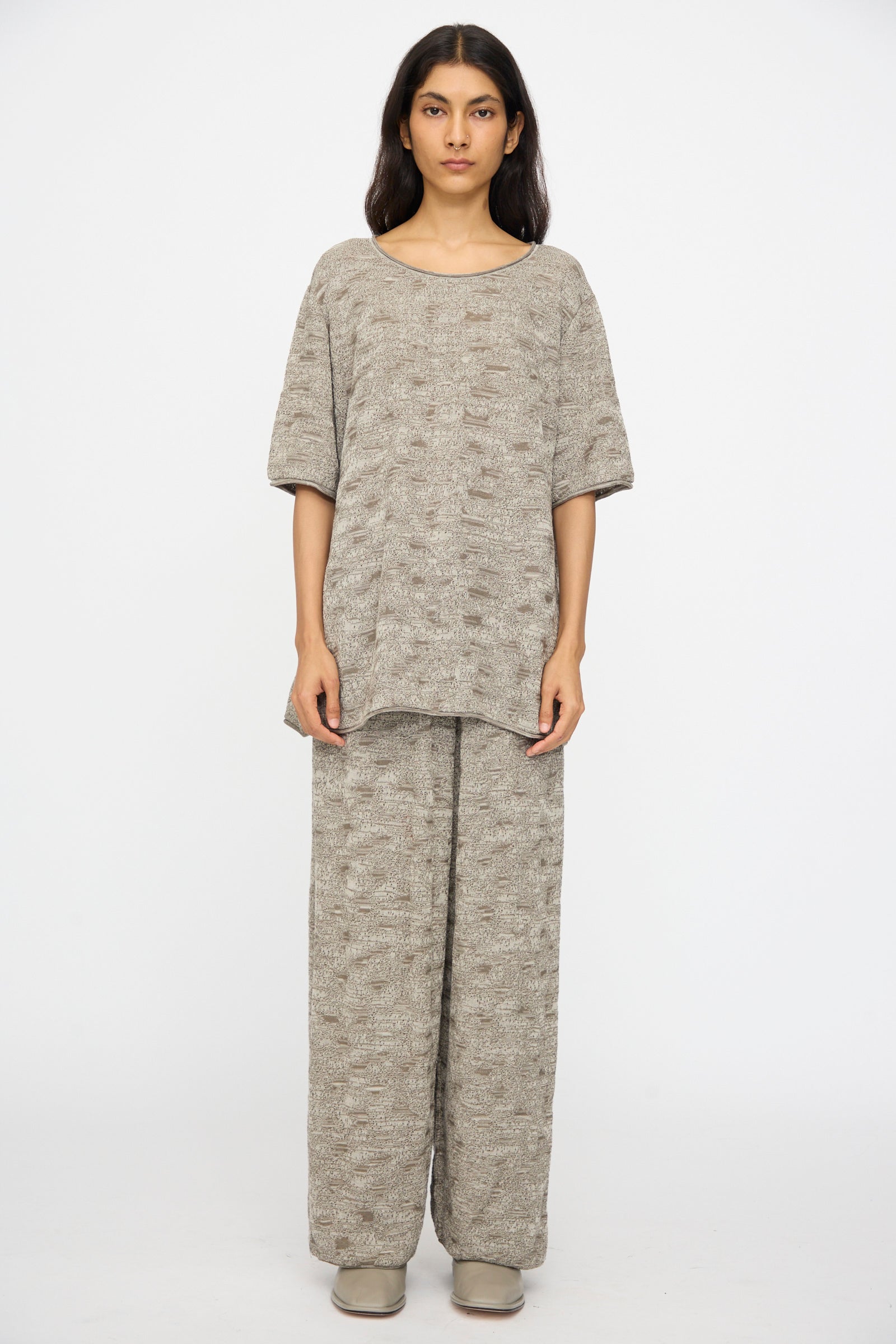 A person faces forward against a plain white background wearing the Lauren Manoogian Terra Tee in Rock Marl with coordinating wide-leg pants and neutral shoes.