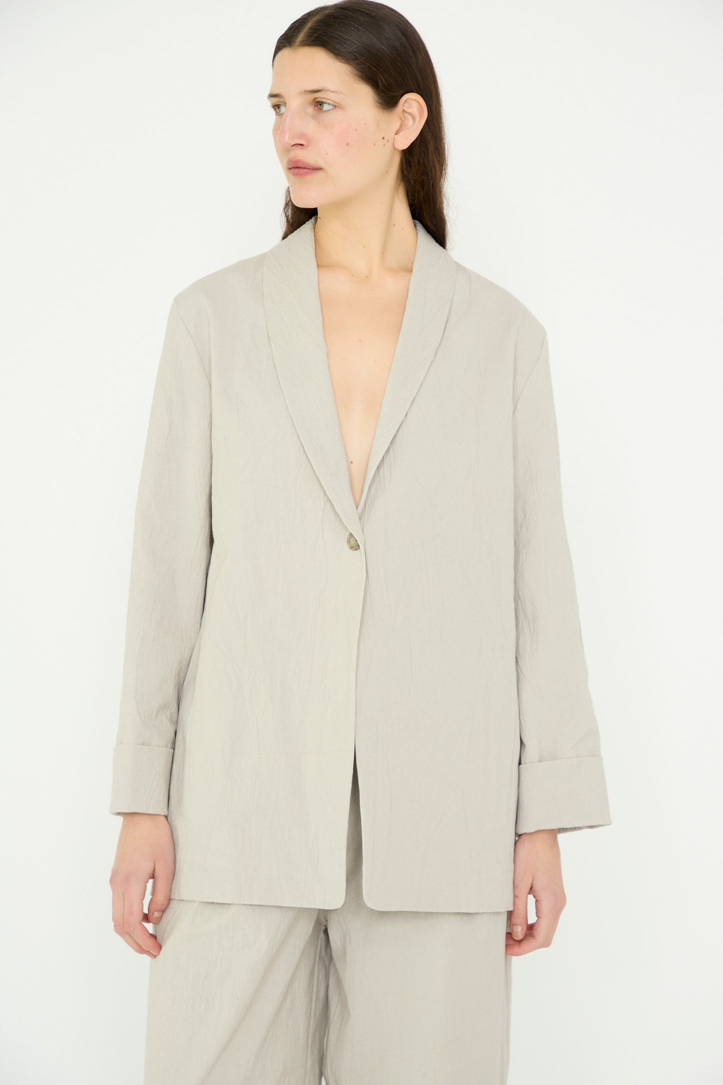 A person wears a Texture Blazer in Pewter by Lauren Manoogian, featuring an open jacket, shawl collar, and rolled sleeves. They look to the side against a white background.