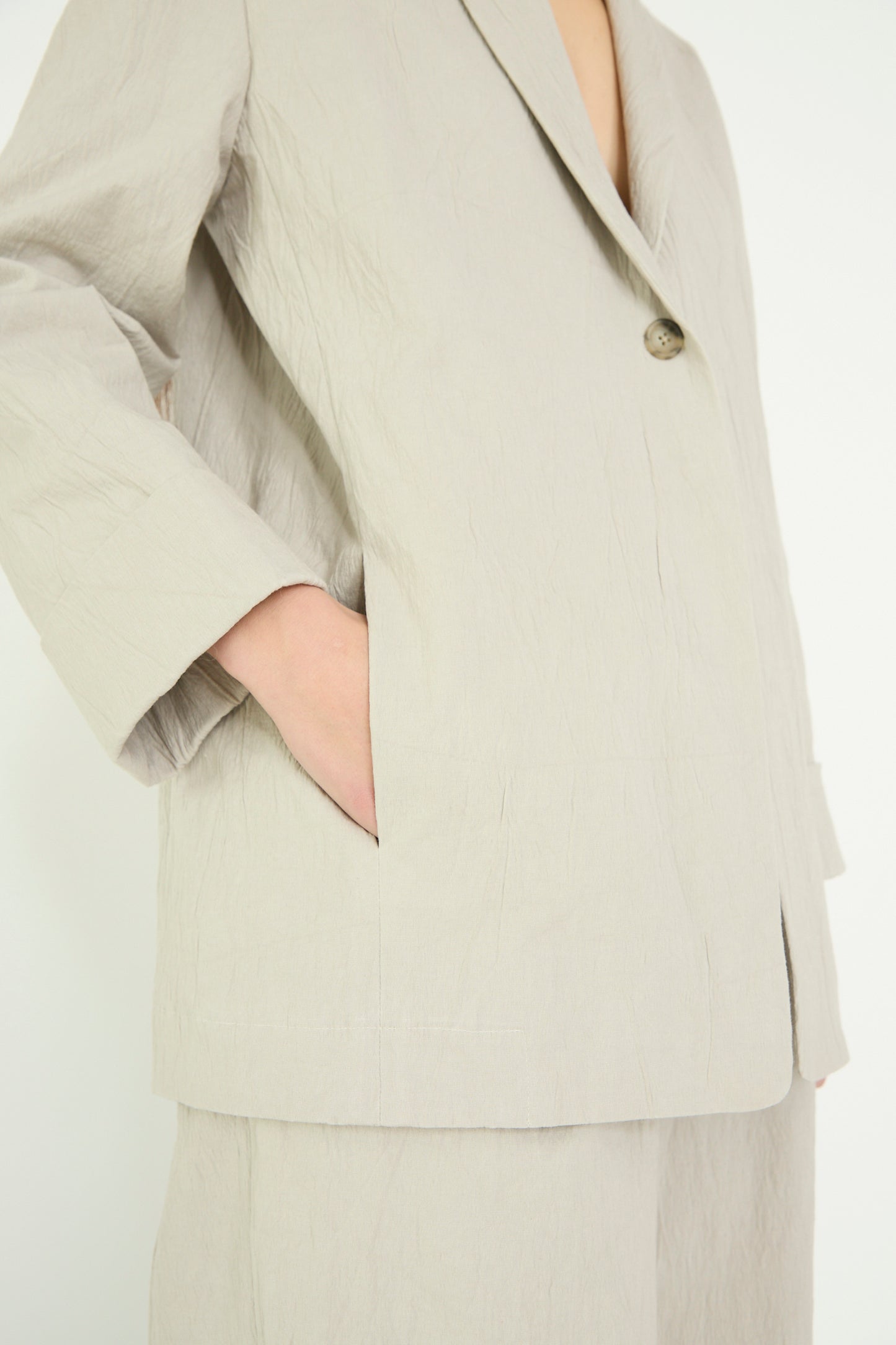 A close-up of a person posing against a plain background, wearing the pewter Texture Blazer with a shawl collar by Lauren Manoogian, one hand casually tucked in the pocket.