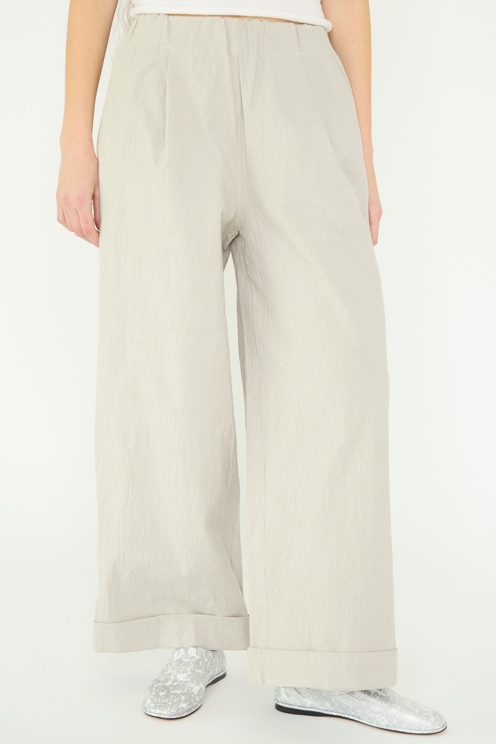 A person is standing against a plain white background, wearing Lauren Manoogian's Texture Trouser in Pewter paired with metallic silver shoes, seen from below the waist. 