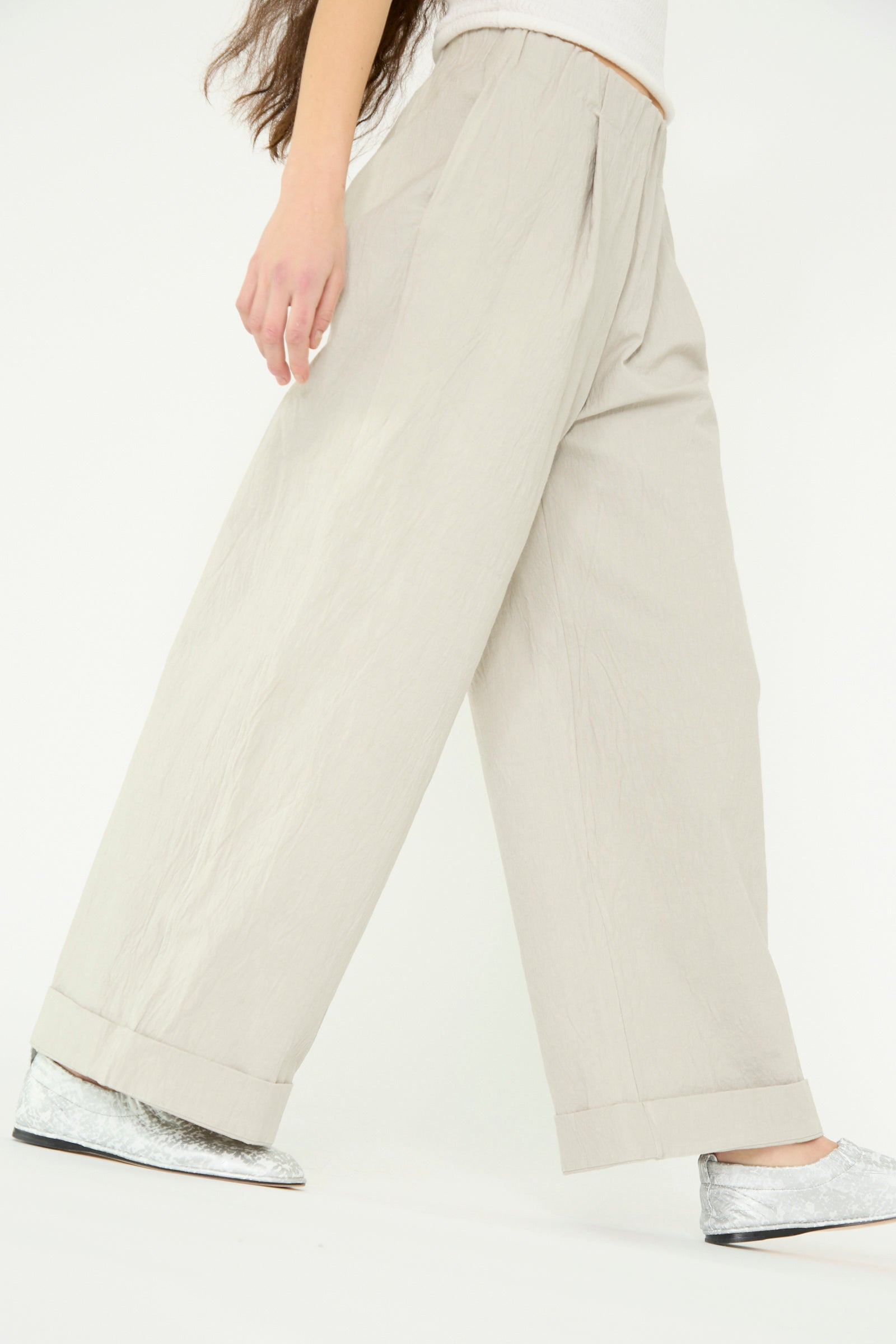 A person wearing Lauren Manoogian's Texture Trouser in a high-waist, wide-leg pewter crinkled cotton blend and silver shoes is shown walking against a plain background.