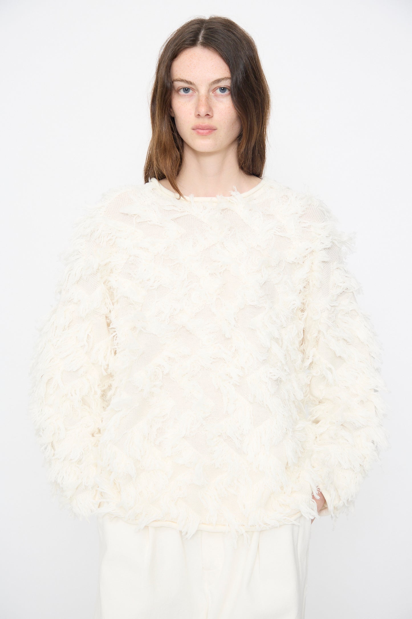 A person with long brown hair wears the Lauren Manoogian Tufted Pullover in Bone with white pants, standing against a plain white background.