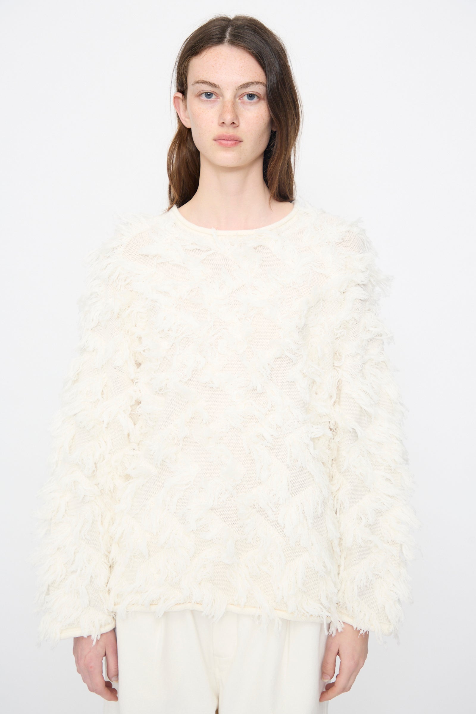 A woman wears the Lauren Manoogian Tufted Pullover in Bone, featuring a textured, oversized design, paired with matching cream pants against a white background.