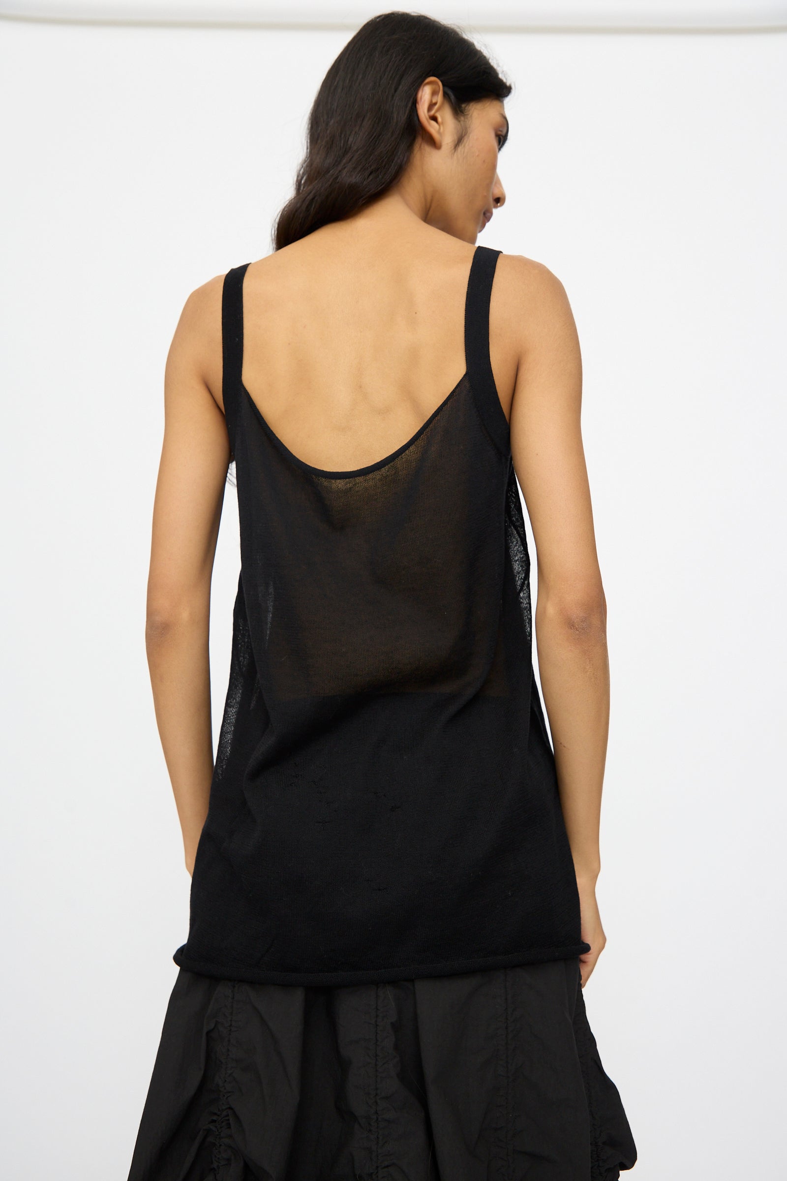 A person stands with their back to the camera, wearing the Lauren Manoogian Veil Camisole in Black and a black pima cotton skirt, set against a plain white background.