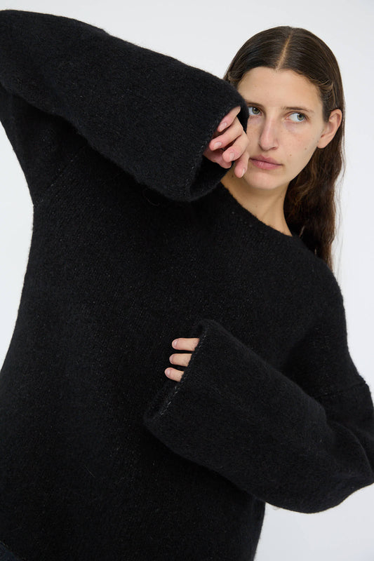 Wearing the Vello Crewneck in Black by Lauren Manoogian, a person with oversized sleeves crafted from luxurious baby alpaca in Peru gazes to the side against a plain background.