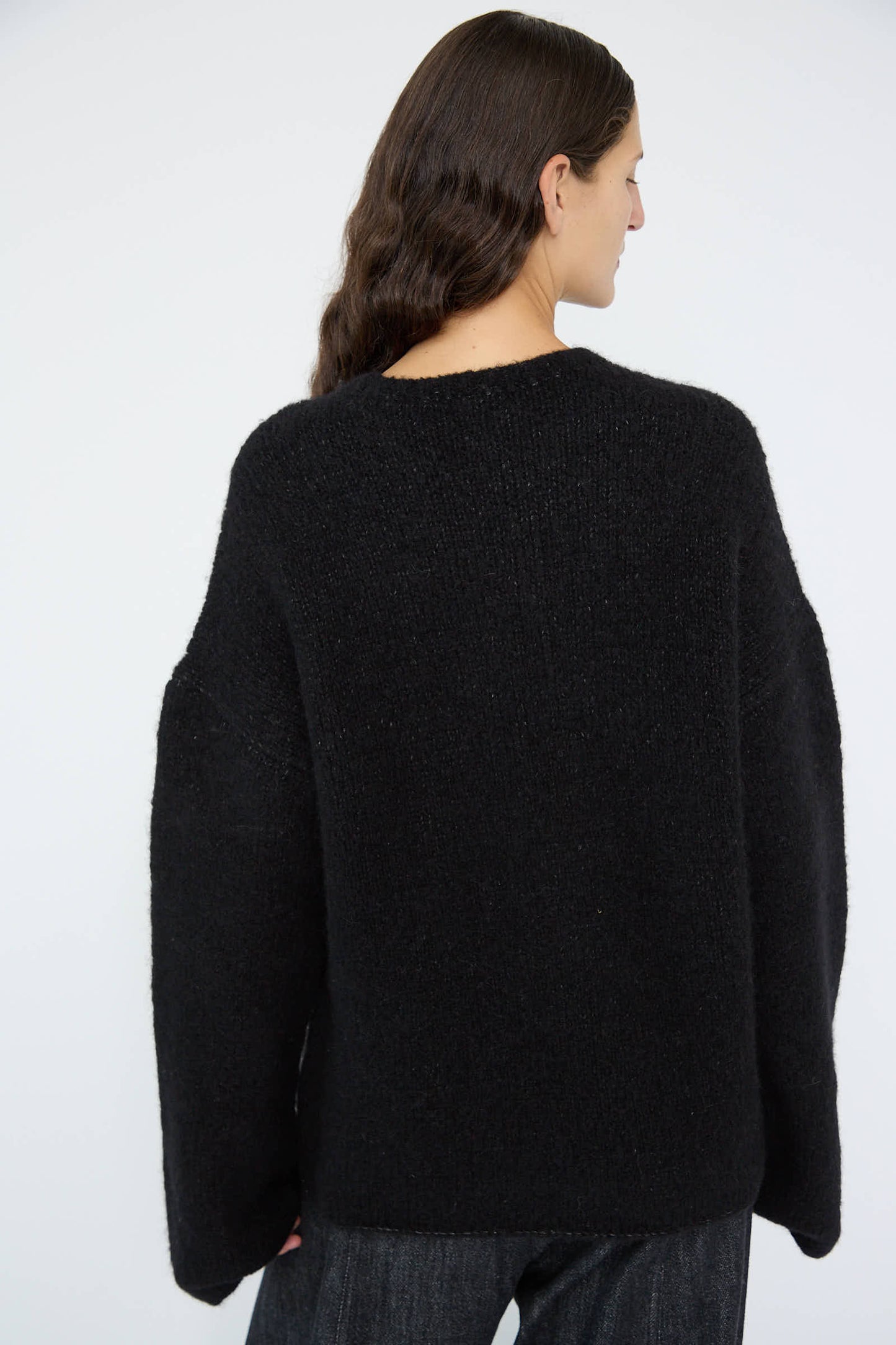 A person with long dark hair is seen from the back wearing the Vello Crewneck in Black by Lauren Manoogian, a loose-fitting knit pullover made in Peru.