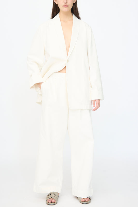 Model wears Lauren Manoogian’s Washed Trouser in White, an oversized relaxed cotton canvas pant with elasticated waist, styled with an open blazer. Hands in pockets, standing against a white background; face partially out of frame.