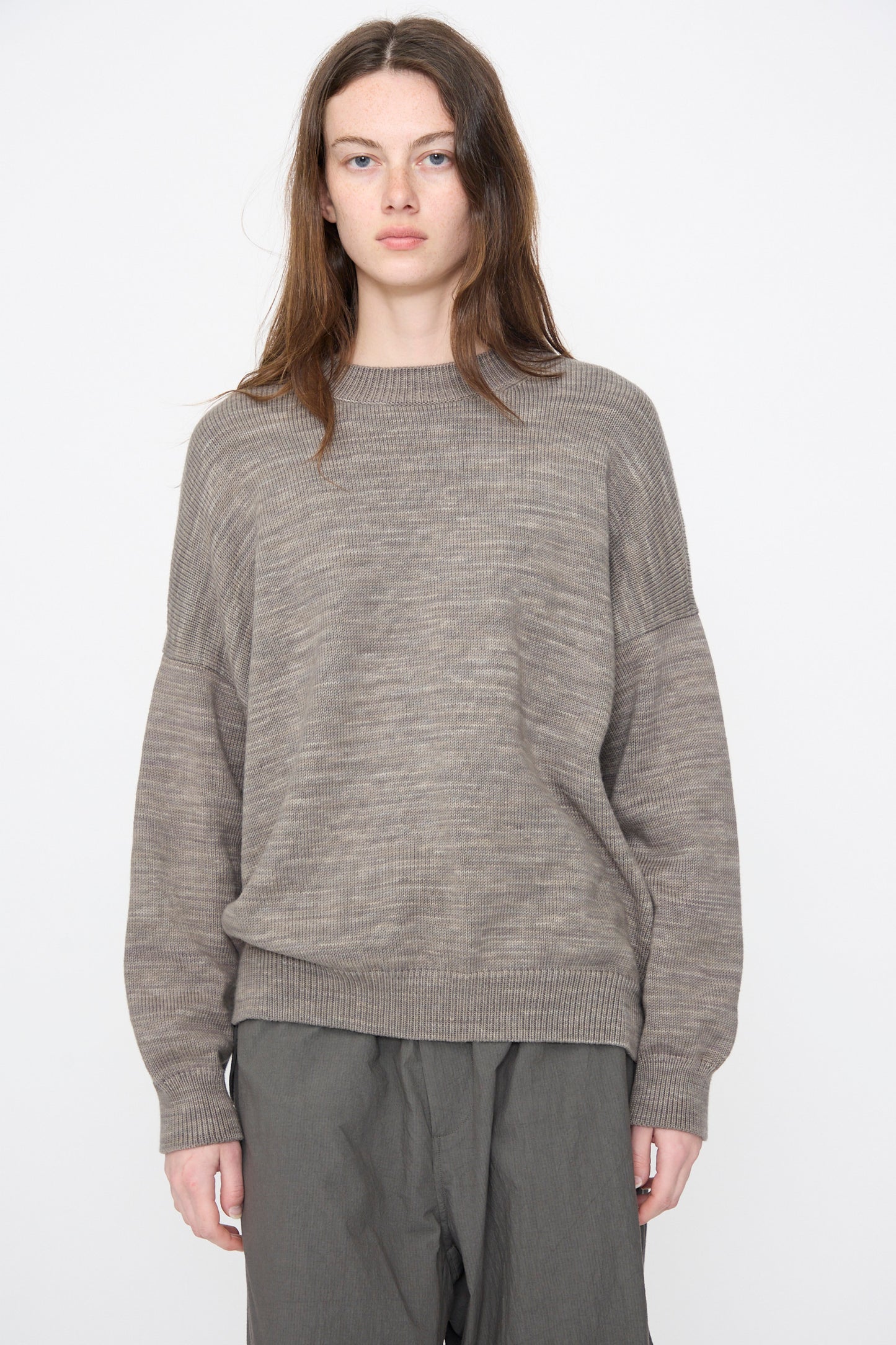 A person with long brown hair wears the Lauren Manoogian Watercolor Crewneck in Rock, paired with gray pants, standing against a plain white background.