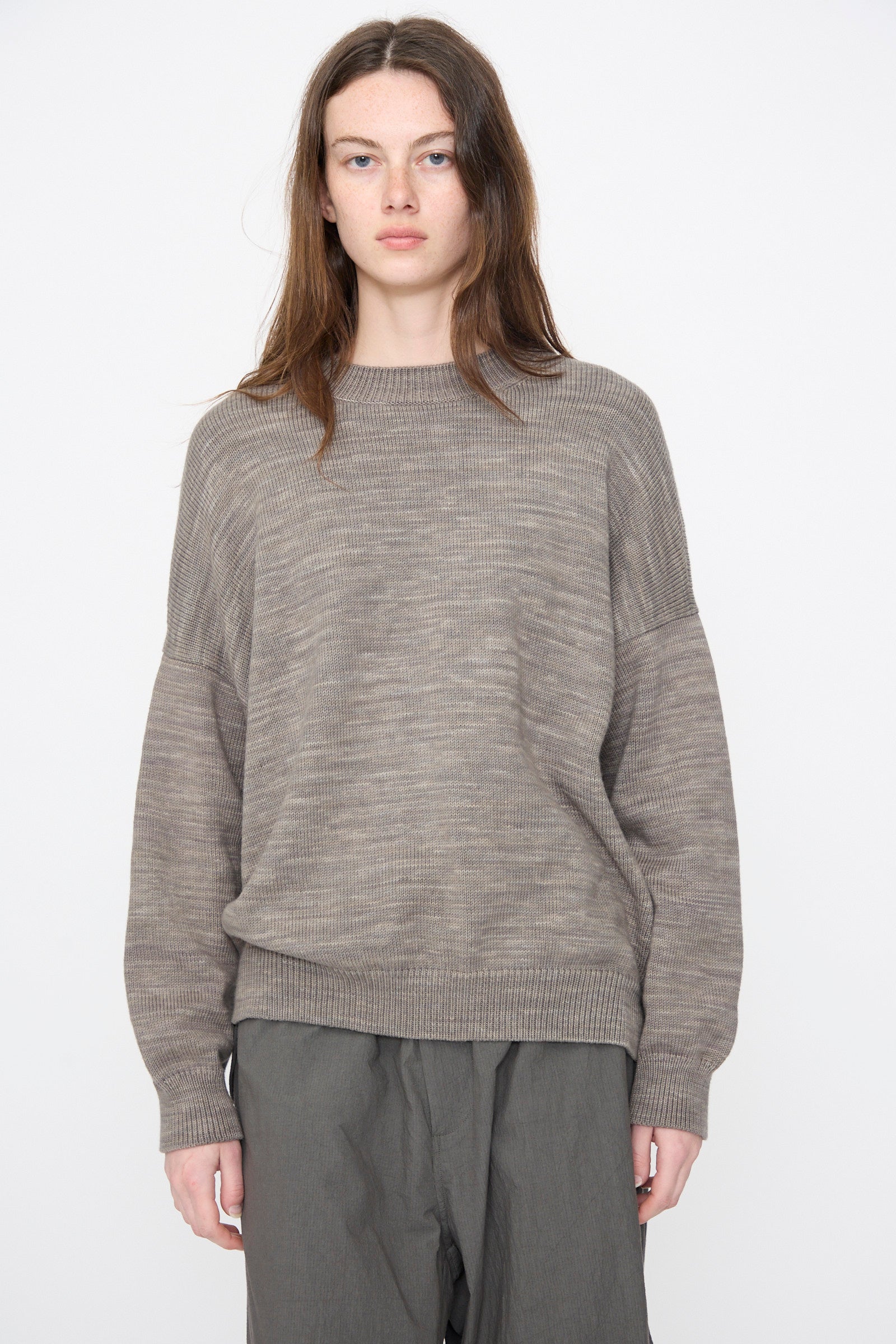 A person with long brown hair wears the Lauren Manoogian Watercolor Crewneck in Rock, paired with gray pants, standing against a plain white background.