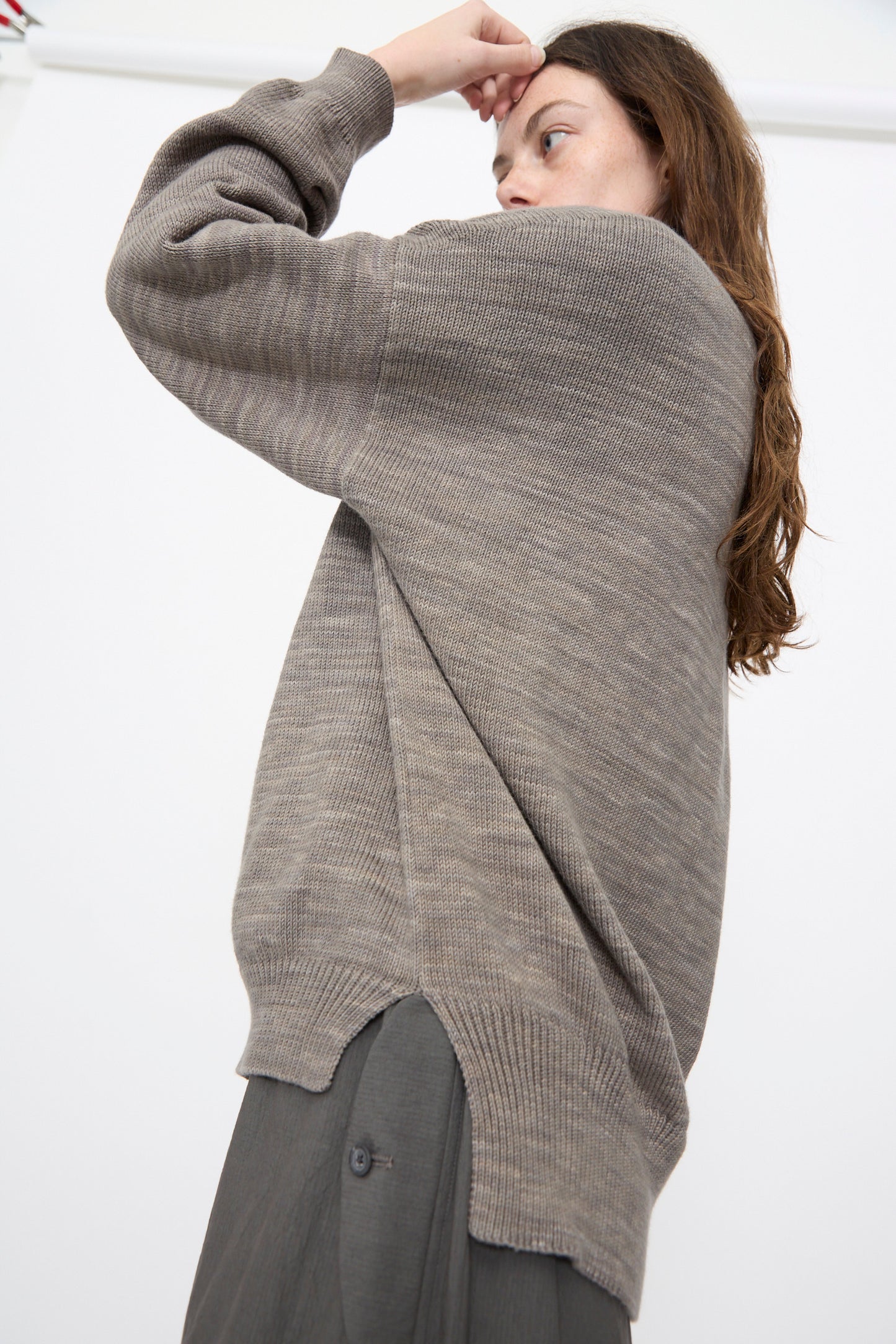Person wearing the Lauren Manoogian Watercolor Crewneck in Rock, a relaxed fit textured cotton knit sweater, paired with gray pants, standing sideways with one arm raised near their forehead against a plain white background.