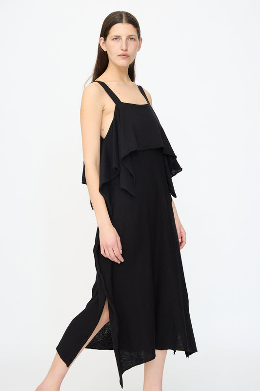 A woman poses against a white background wearing the Lauren Manoogian Wave Dress in Black, a sleeveless cotton-linen knit midi dress featuring a ruffled overlay and side slits.