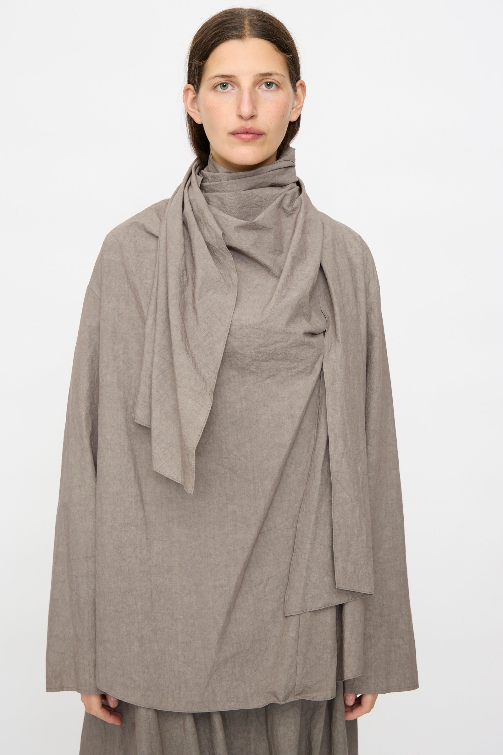 A person faces forward in the Lauren Manoogian Wrap Top in Cinder, a loose long-sleeve cotton piece with a matching scarf draped at the neck. Made in Japan, shown against a plain white background.