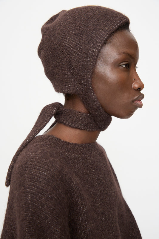 A person in profile wears the Lauren Manoogian Loft Bonnet in Soil, a fitted alpaca blend bonnet with ties, made in Peru, shown against a plain white background.