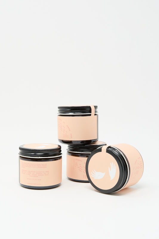 Three small 45ml dark glass jars of Lauren’s All Purpose Rose Vetiver Salve with peach labels and black lids, featuring a white winged logo, are arranged on a white background, suggesting premium vegan skincare.