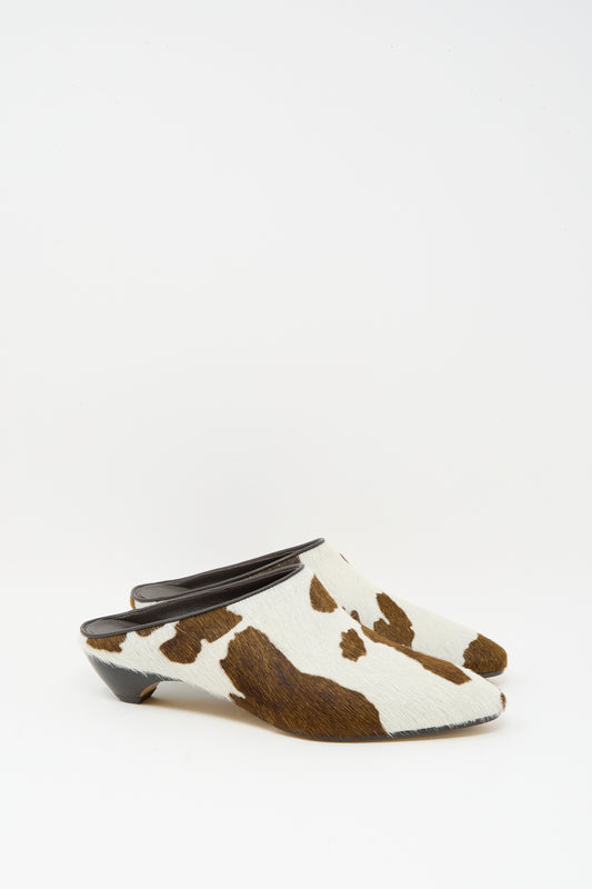 The Le Monde Beryl Allegra Mule in Cow features a low mini heel and calf hair leather upper with a chic brown and white cow print, displayed on a white background.