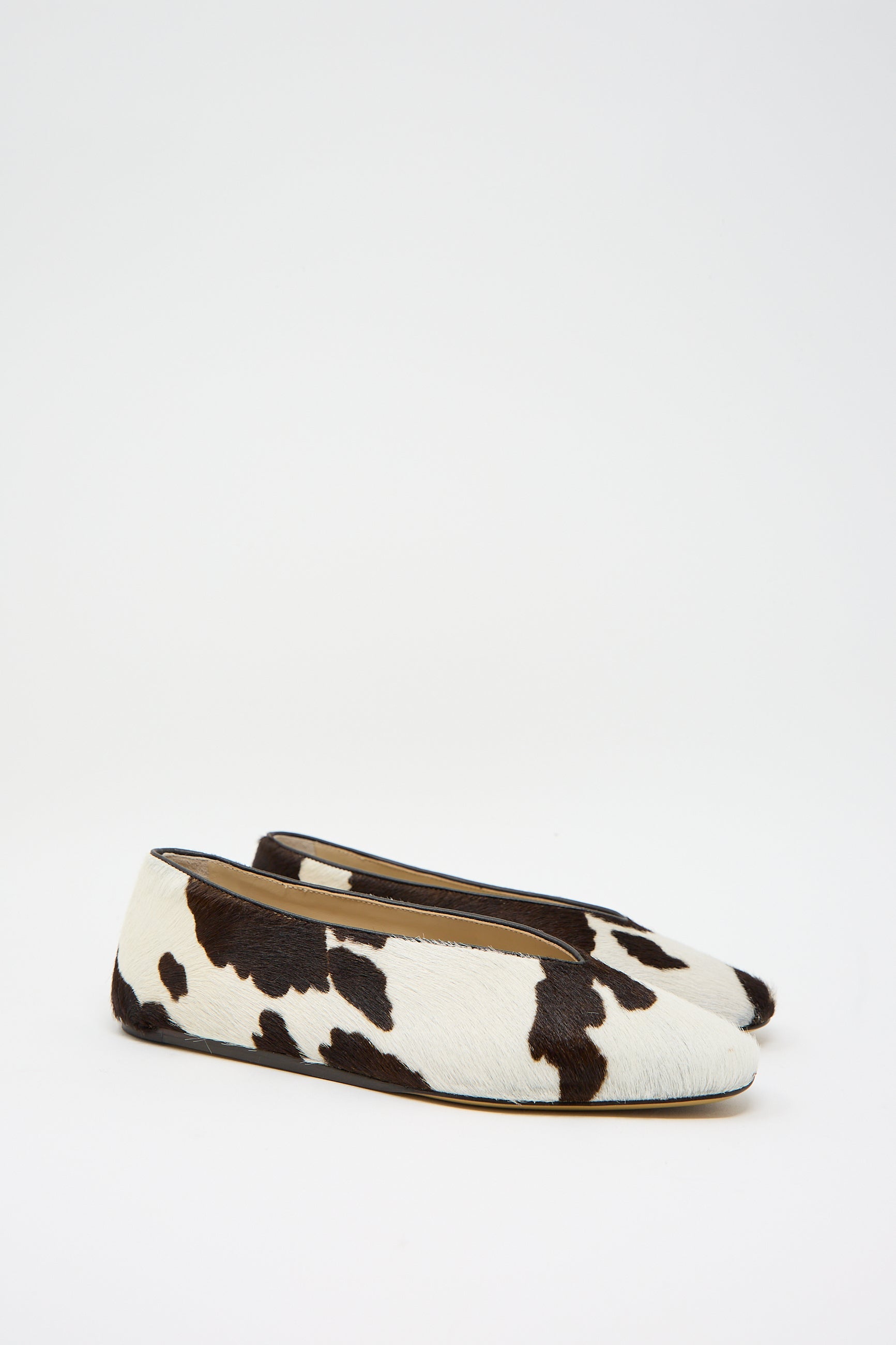 A pair of Le Monde Beryl's Calf Hair Regency Slipper in Cow, featuring elegant leather piping on a white background.