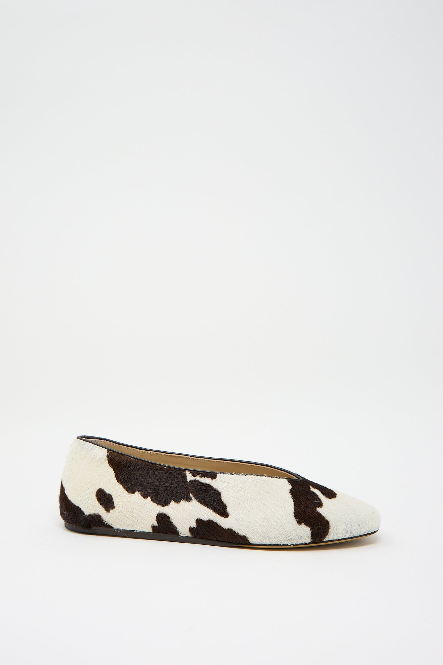 The Calf Hair Regency Slipper in Cow by Le Monde Beryl showcases a stylish cow print pattern on a clean white base, enhanced with sophisticated leather piping.