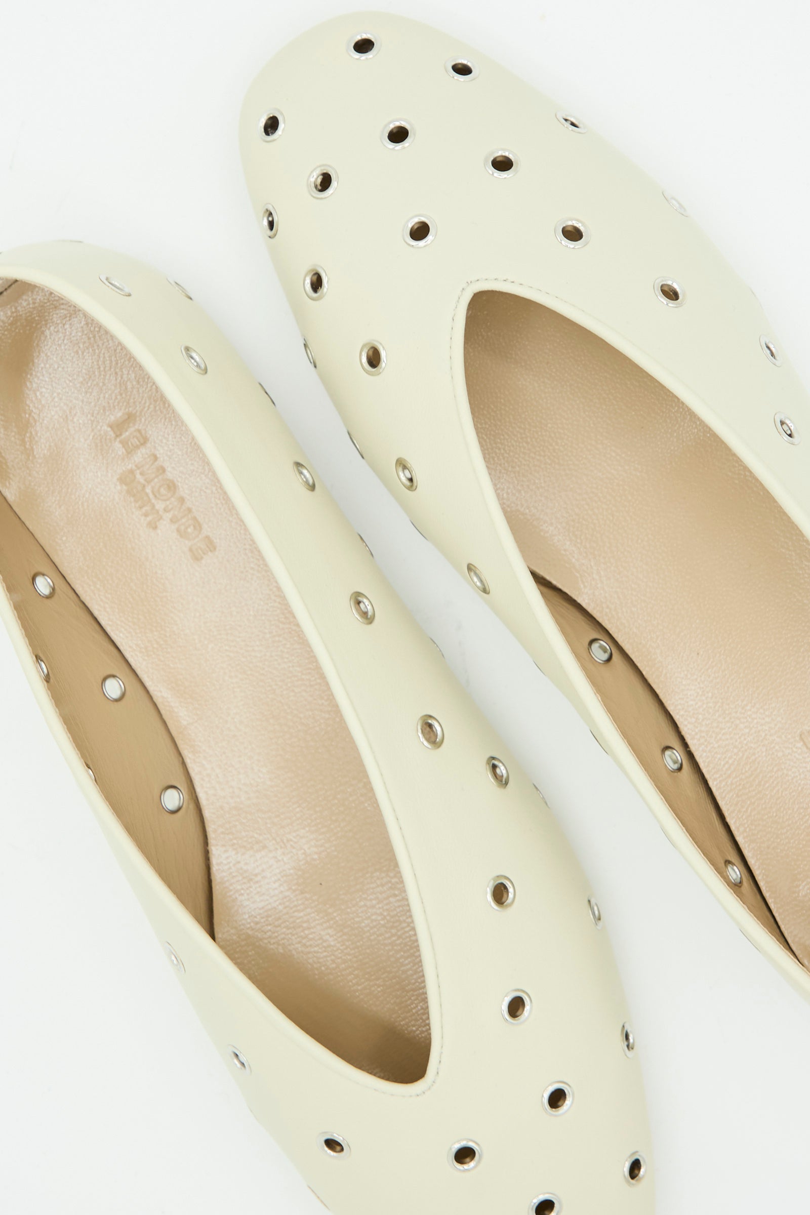 Close-up of Le Monde Beryl's Eyelet Studded Leather Regency Slipper in Ecru, featuring silver grommet holes and cushioned insoles, shown on a white background.