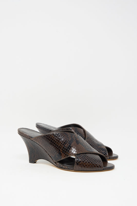 The Luca Mule in Snake Chocolate by Le Monde Beryl features dark brown, open-toe wedge sandals made of luxurious calf leather with a shiny snakeskin finish, shown against a white background.