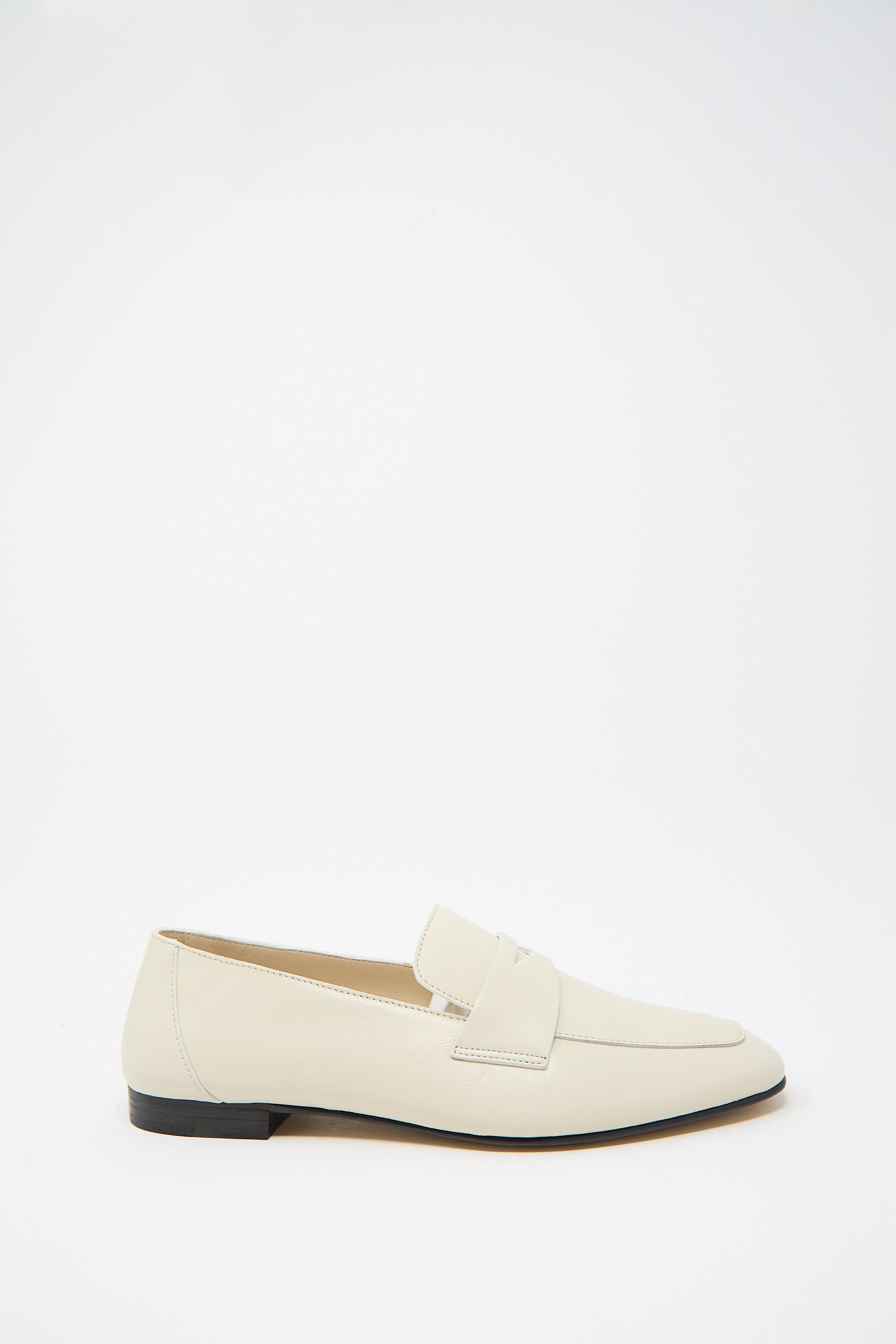 A single white lambskin loafer with a cushioned insole and a 10mm black heel, featuring a strap detail across the top, displayed against a plain white background is the Soft Loafer with Placket in Ecru by Le Monde Beryl.