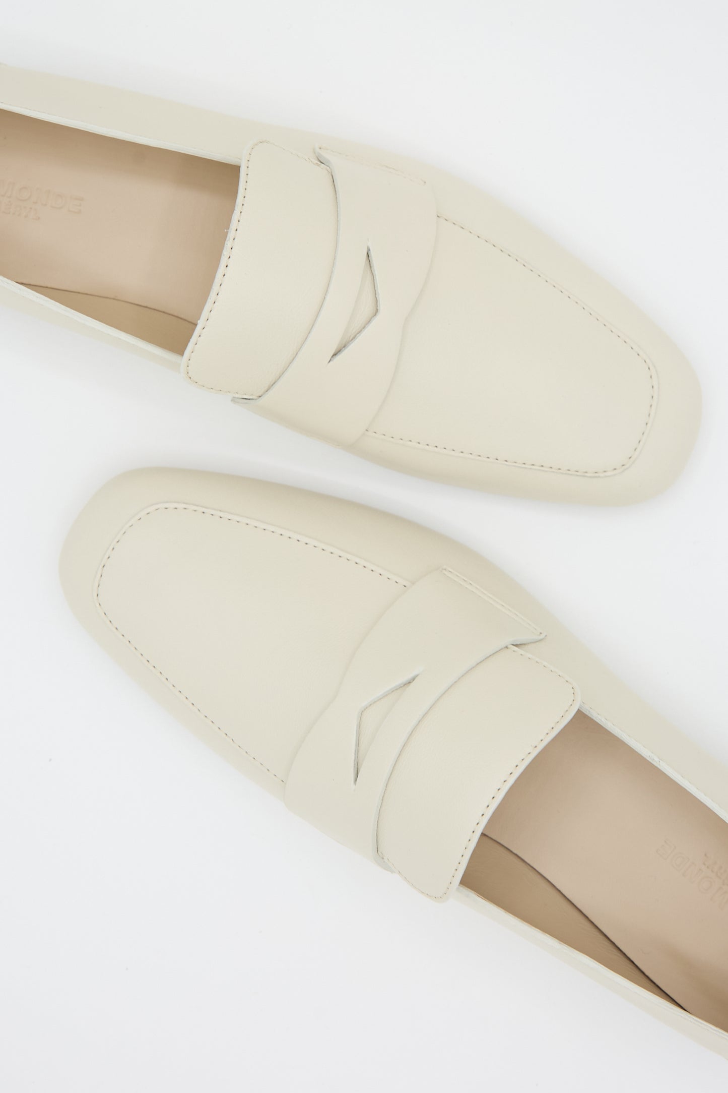 A pair of Soft Loafers with Placket in Ecru from Le Monde Beryl with stitched detailing and a small triangular cutout on the strap, viewed from above on a white background.