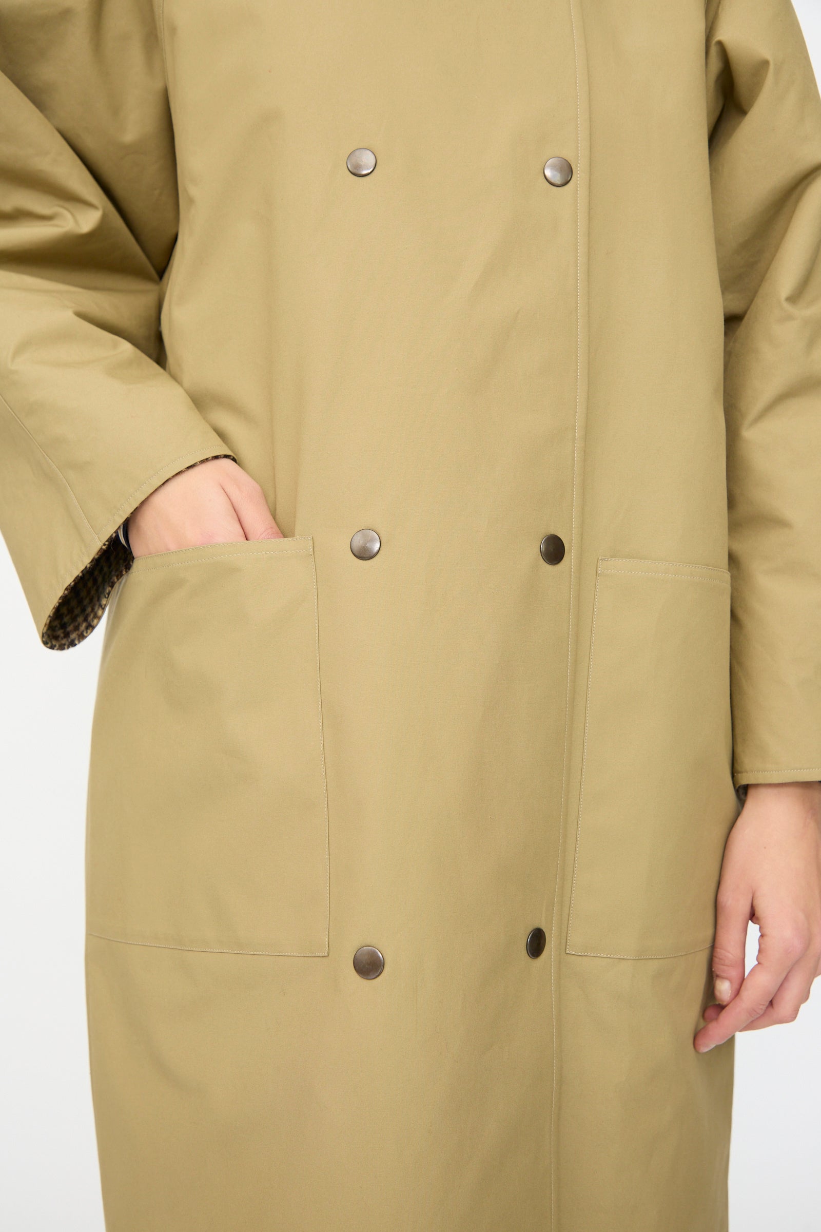 A person wearing the Les Prairies De Paris Dickens Moon Reversible British Trench in Taupe, with large front pockets and one hand tucked inside a pocket.
