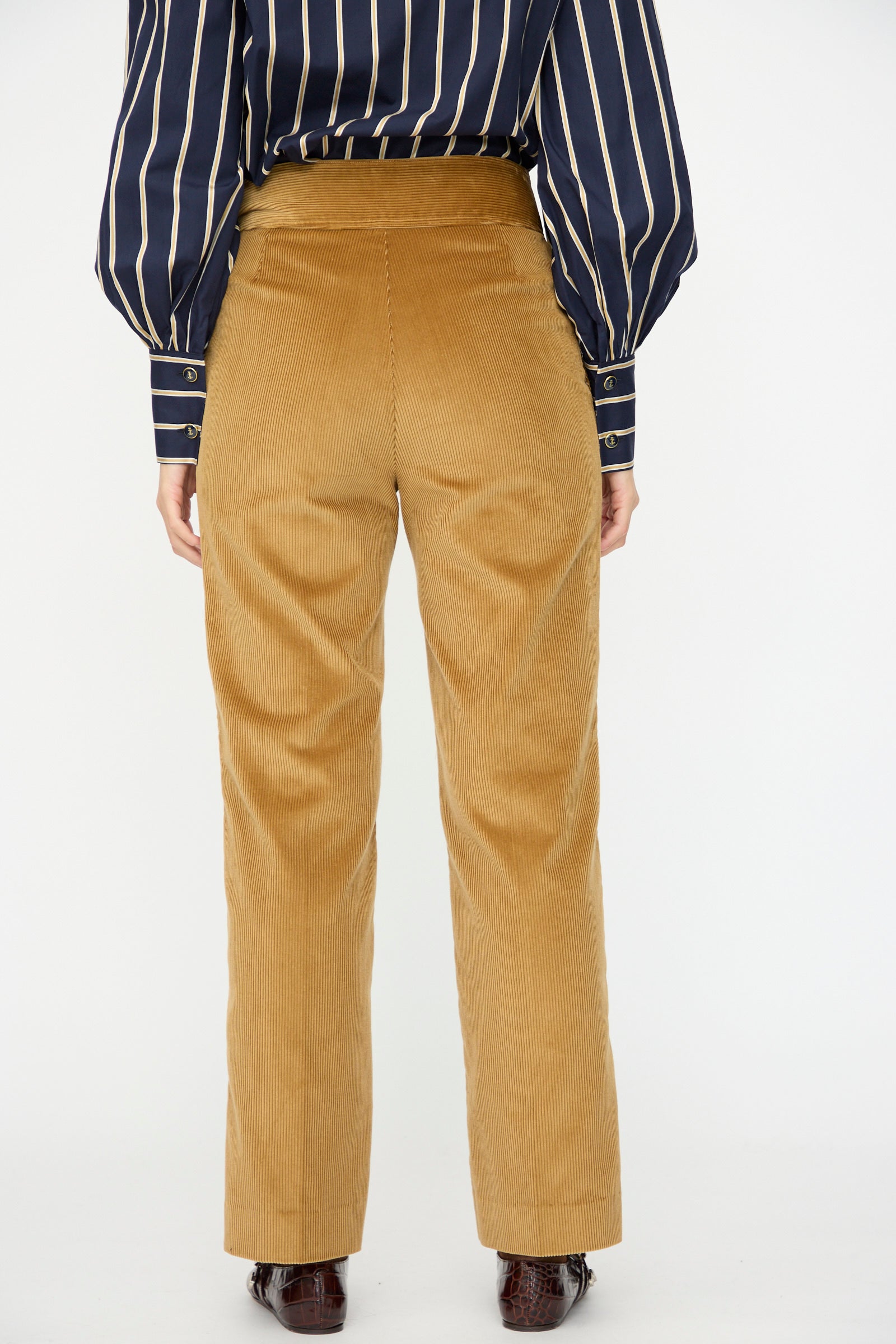 Model wears the Gaoutcho Trouser in Miel by Les Prairies De Paris with a navy, long-sleeve striped shirt, shown from the back against a plain white background.