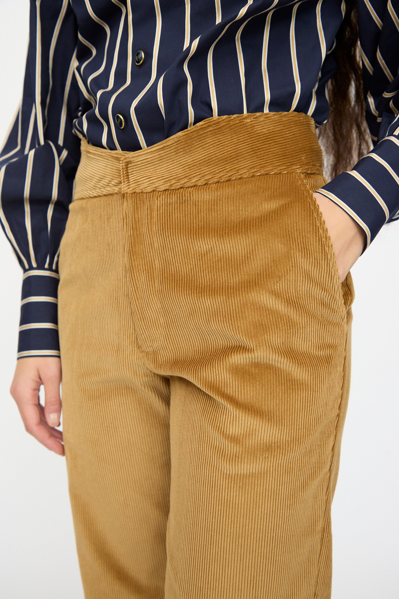 Person wearing navy and white striped shirt tucked into Les Prairies De Paris Gaoutcho Trouser in Miel, with hands in pockets.