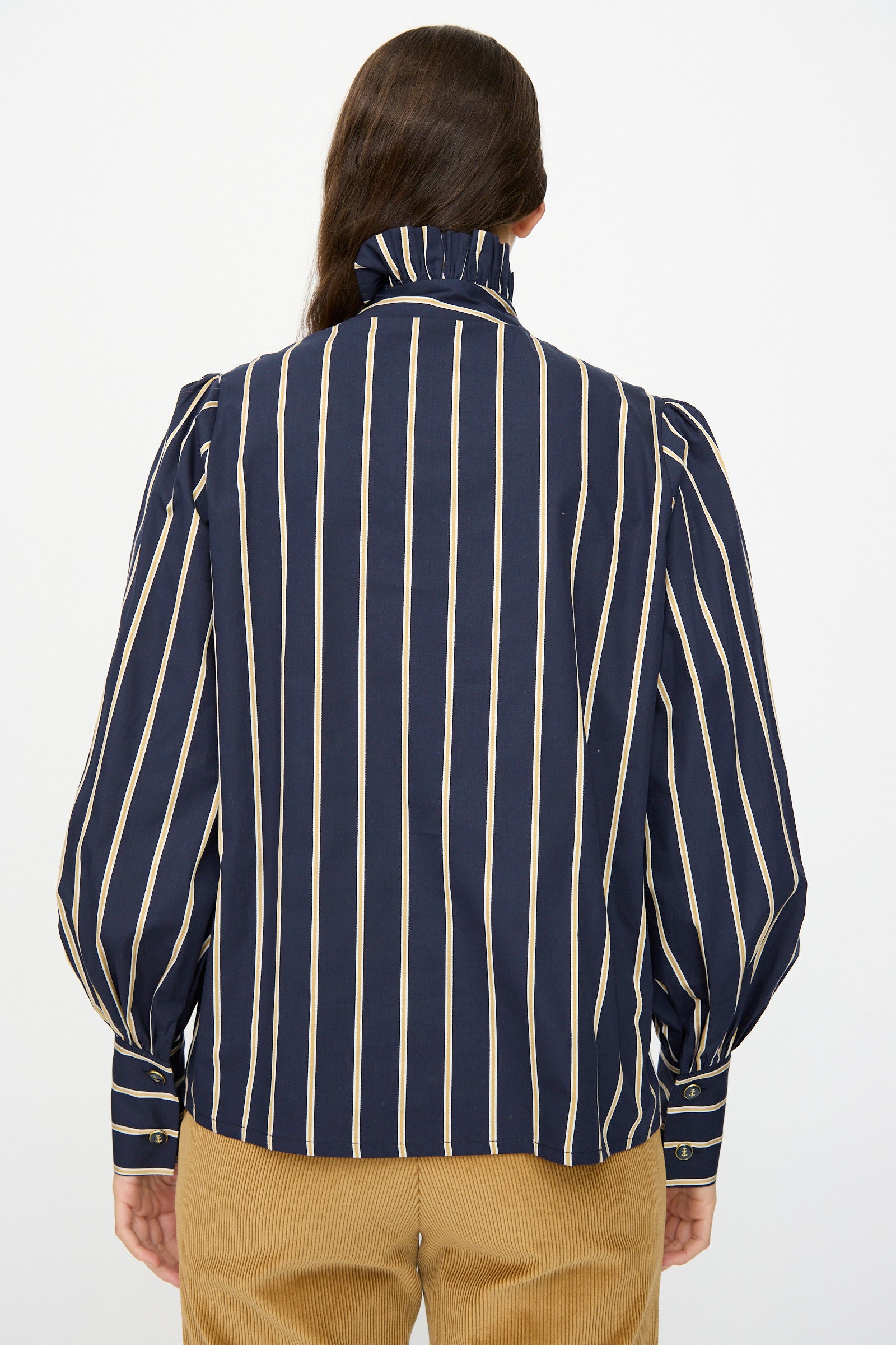 A person is seen from behind wearing the Les Prairies De Paris Cotton Josephine Shirt in R Studio, a navy striped cotton shirt with puff sleeves, paired with light brown corduroy pants.