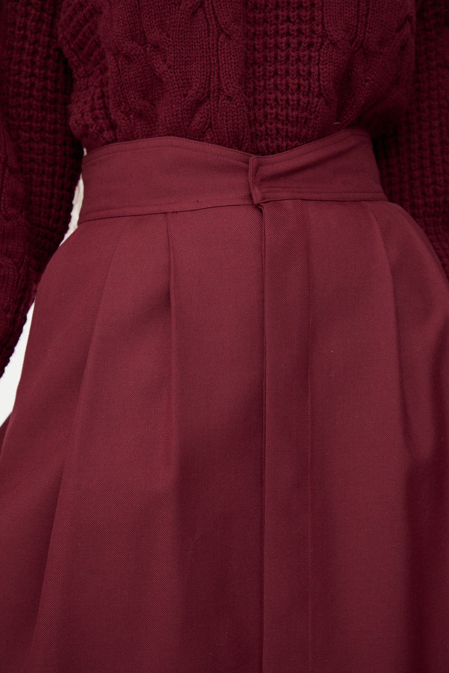Close-up of a person wearing a textured maroon sweater tucked into the Les Prairies De Paris Twill Georgie Skirt in Bordeaux.