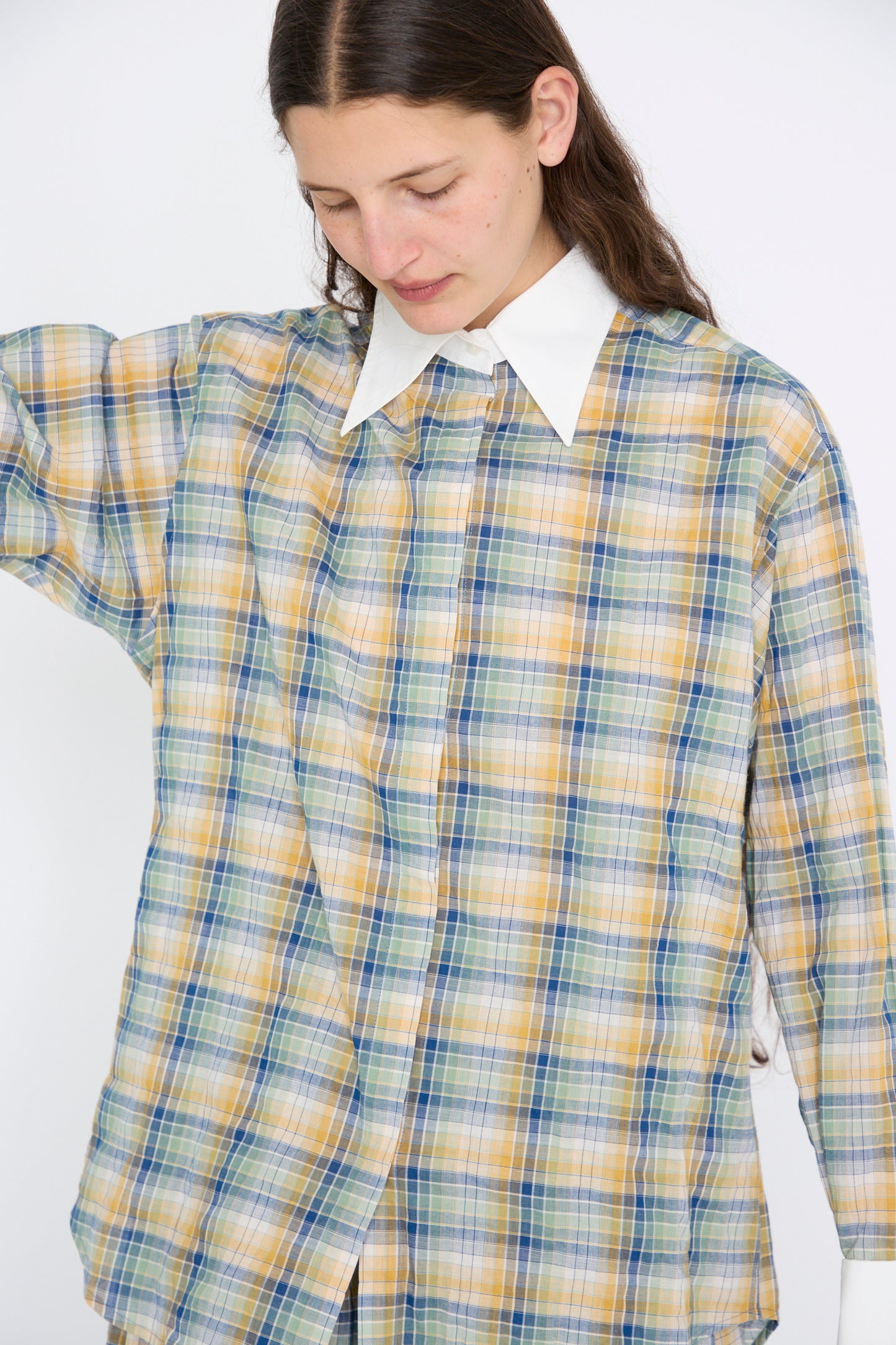 A person wearing the Chemise Oxford in Paper Miel by Les Prairies De Paris, featuring a large plaid design with an oversized white collar, looks down.