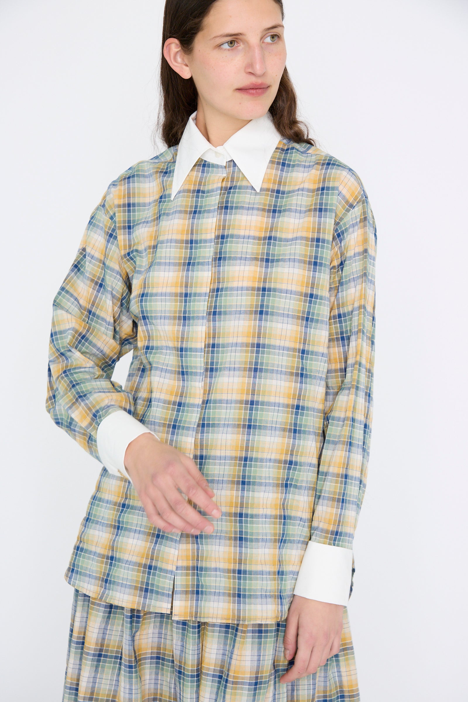 A person wearing the Chemise Oxford in Paper Miel by Les Prairies De Paris, featuring a plaid design with a white collar and cuffs, gazes to the side against a plain background.