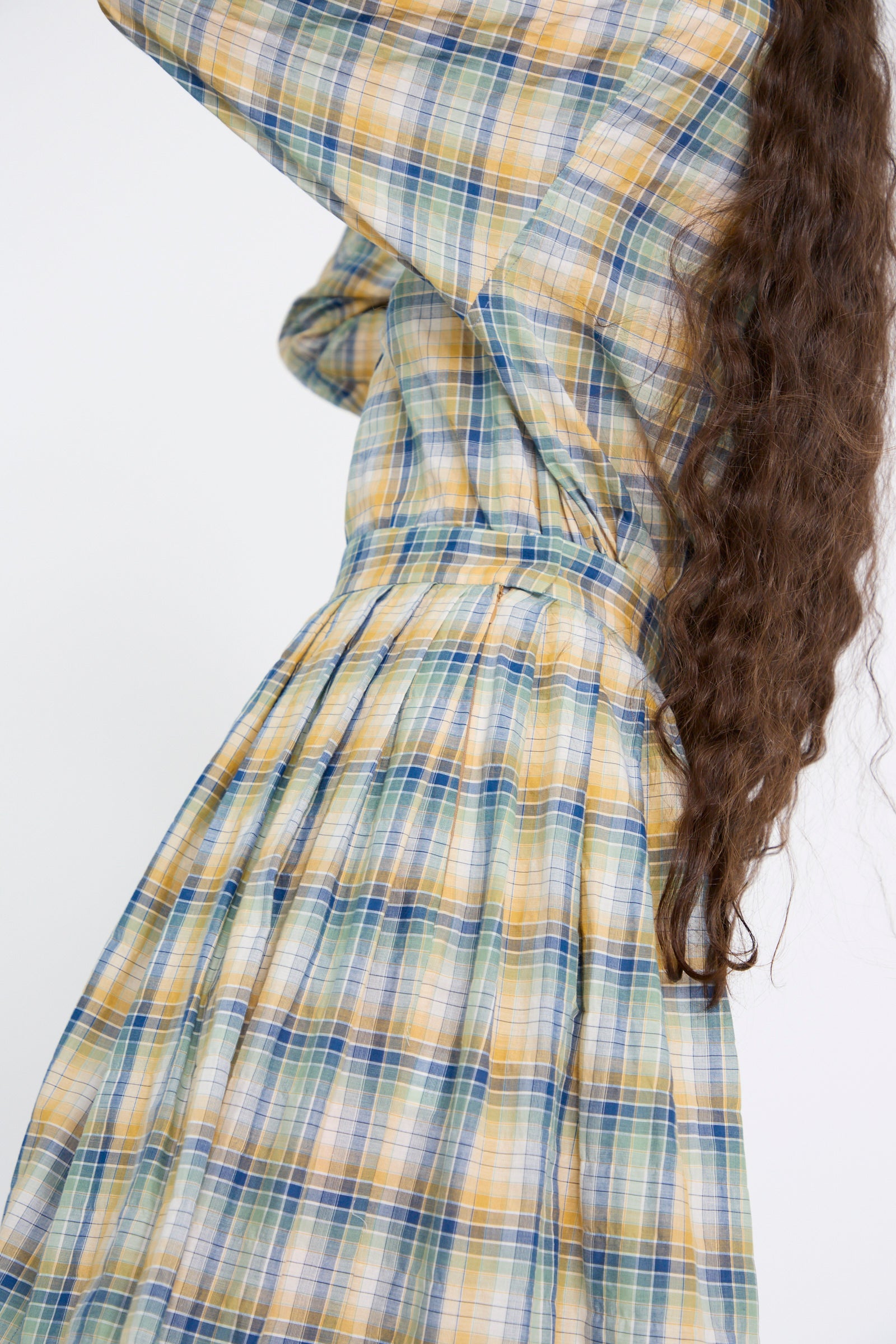 A person showcases long, wavy brown hair while wearing the Jupe Roberta in Paper Miel from Les Prairies De Paris, featuring a plaid cotton pattern in harmonious green, blue, and yellow tones.