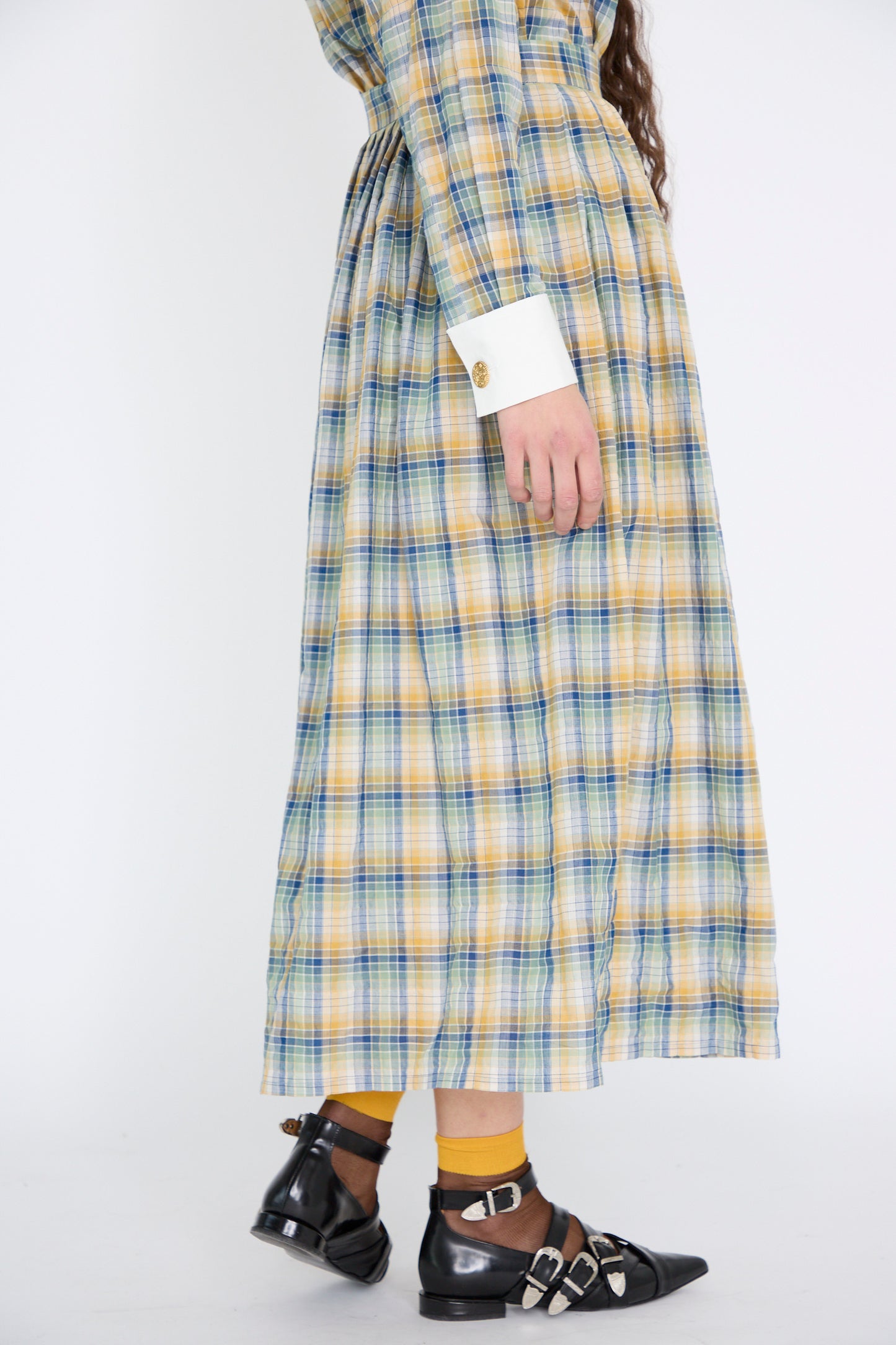 A person in the Les Prairies De Paris Jupe Roberta in Paper Miel dress paired with yellow socks and black buckle shoes walks against a plain backdrop.